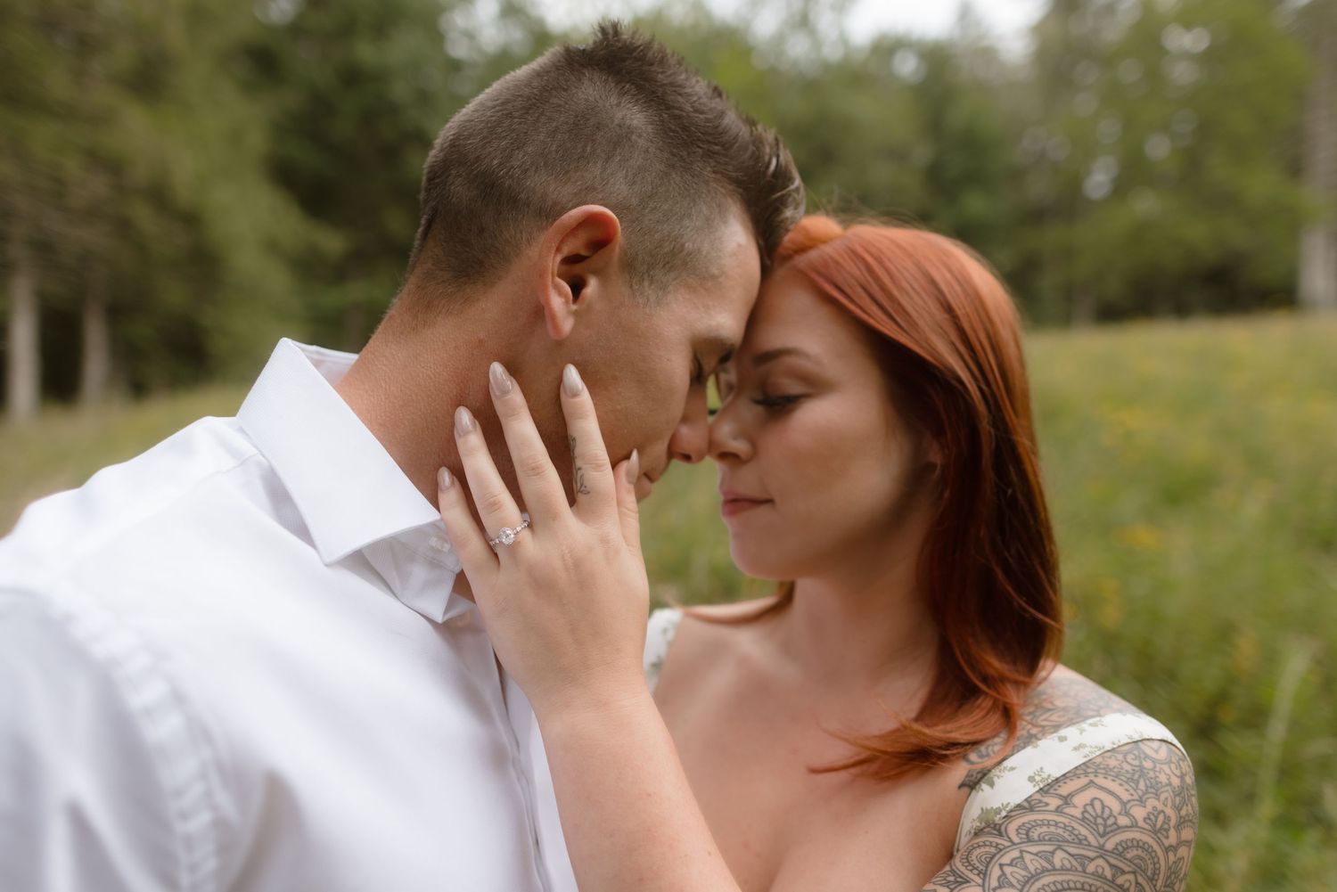 A tender intimate moment between two people in a natural outdoor setting, touching faces while wearing white clothing.