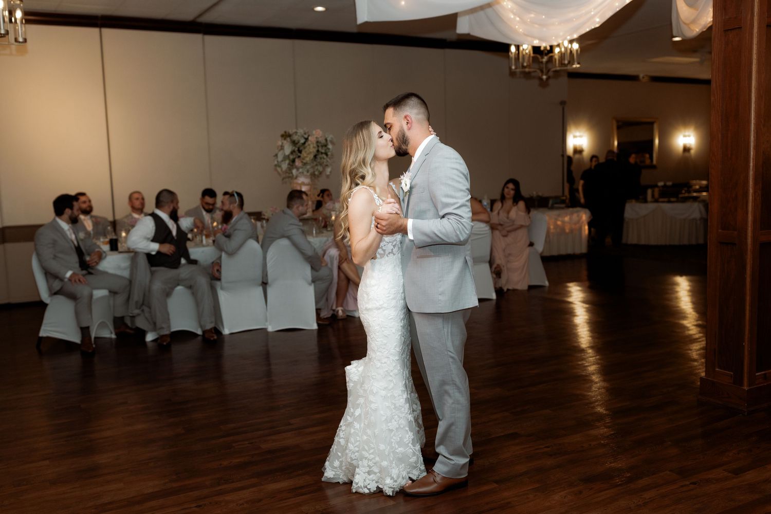 Bride and groom share their first dance surrounded by guests at wedding reception.