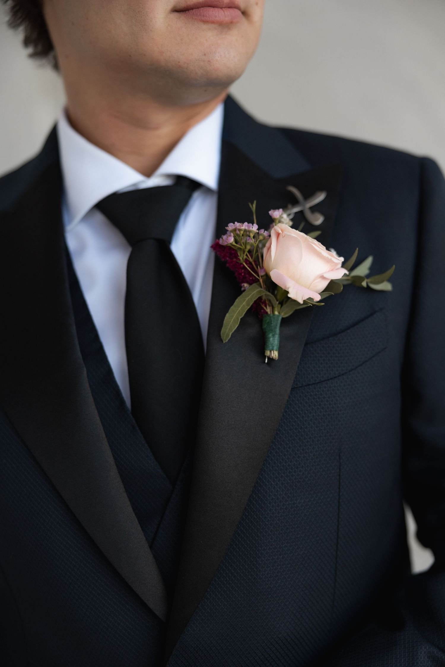 Close-up of elegant black tuxedo suit with blush pink rose boutonniere and dark tie.