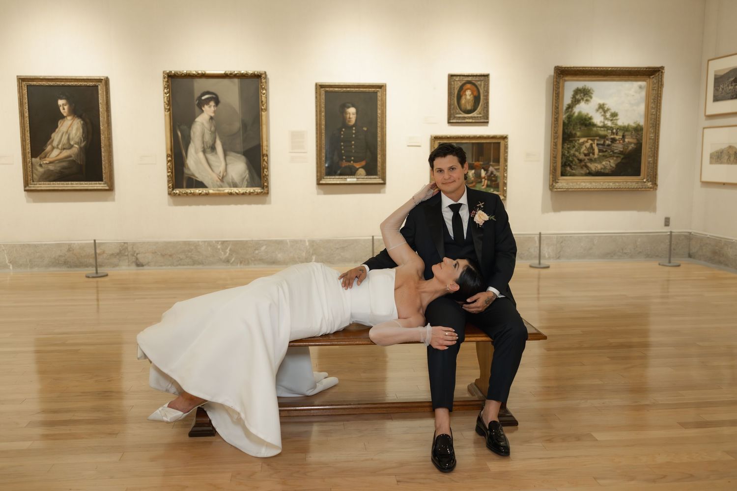 Couple poses playfully in an art gallery with classic paintings and polished hardwood floors during their wedding shoot.