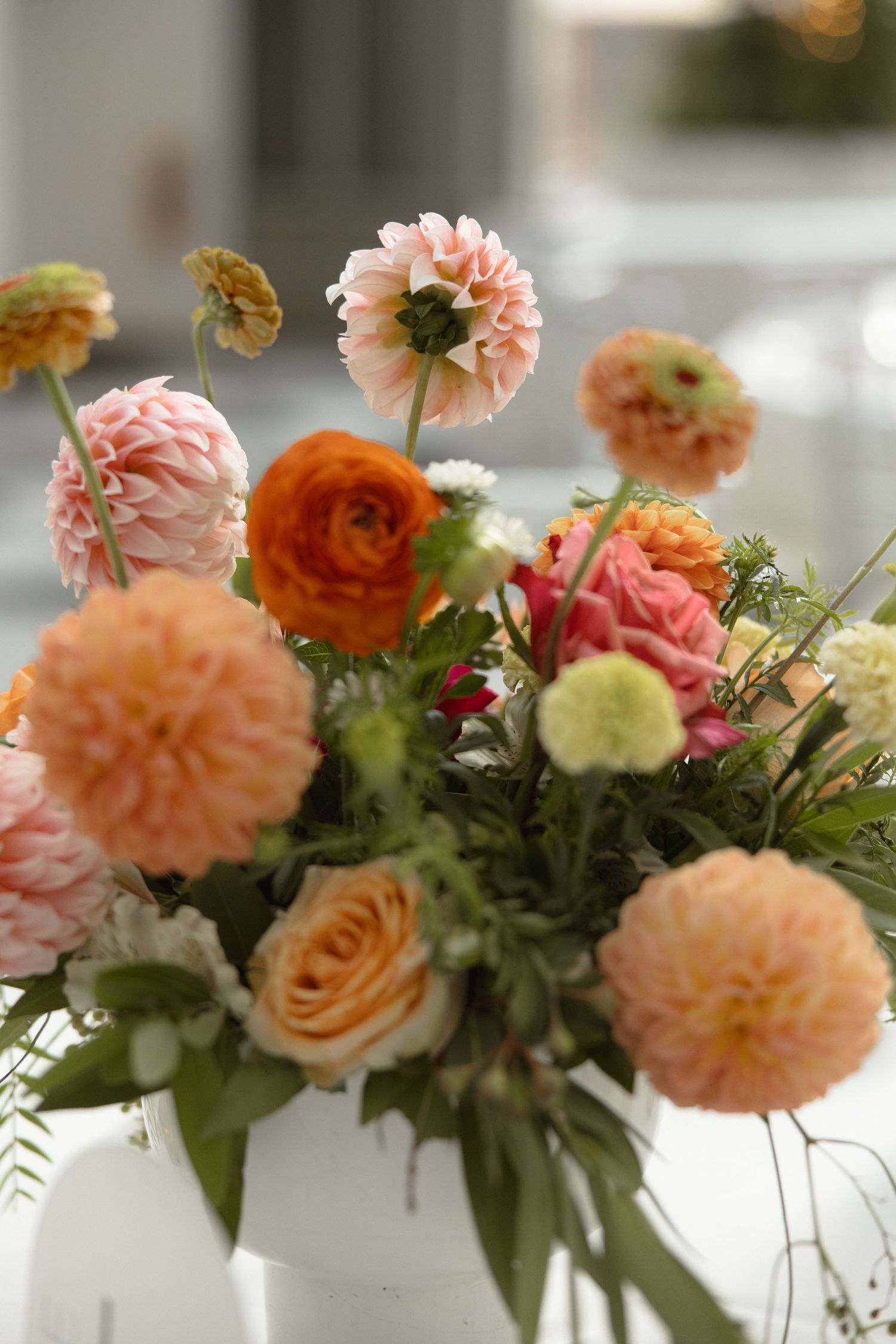 Romantic floral arrangement with coral dahlias, peach roses, and ranunculus in soft natural light.