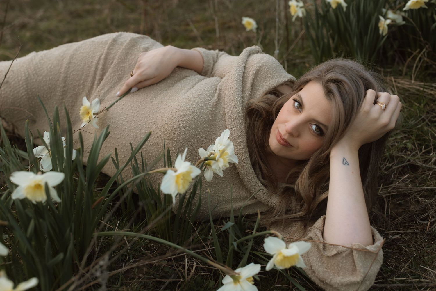 Spring maternity photoshoot with white daffodils and a cozy beige dress.