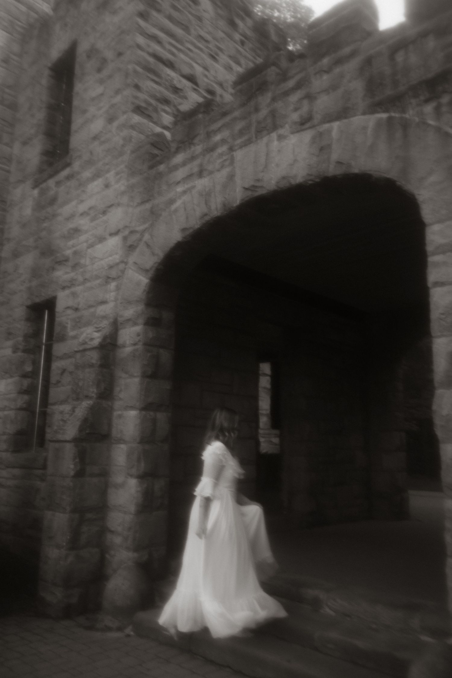 A ghostly figure in a flowing white dress stands beneath a stone archway of an ancient castle or church in black and white.