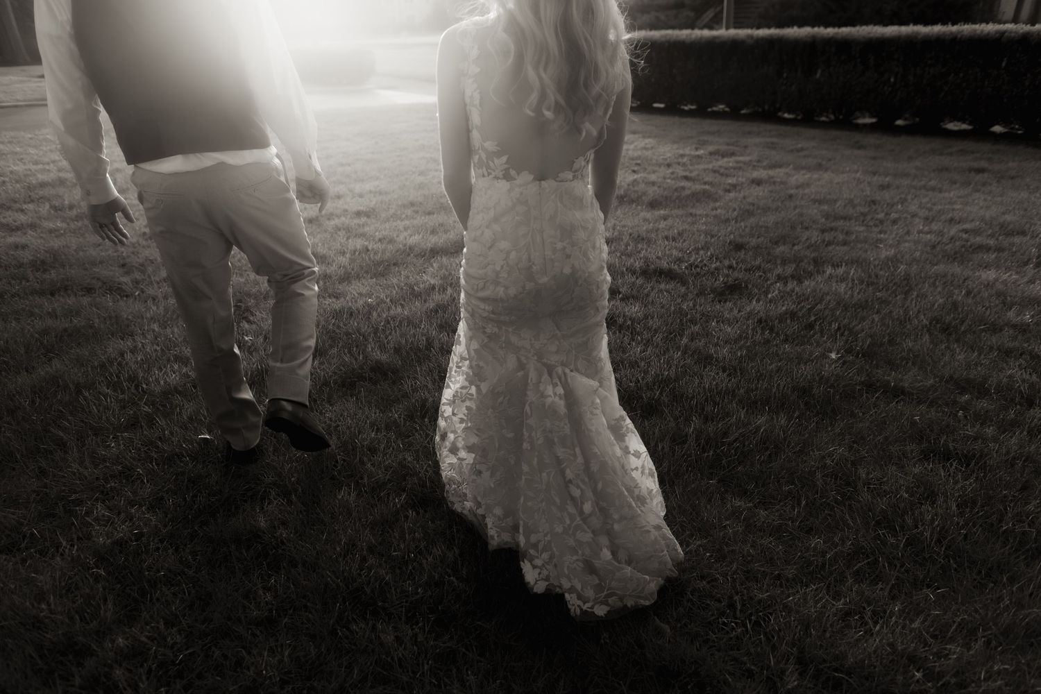 Black and white photo showing the bottom half of a couple standing on grass in wedding attire.