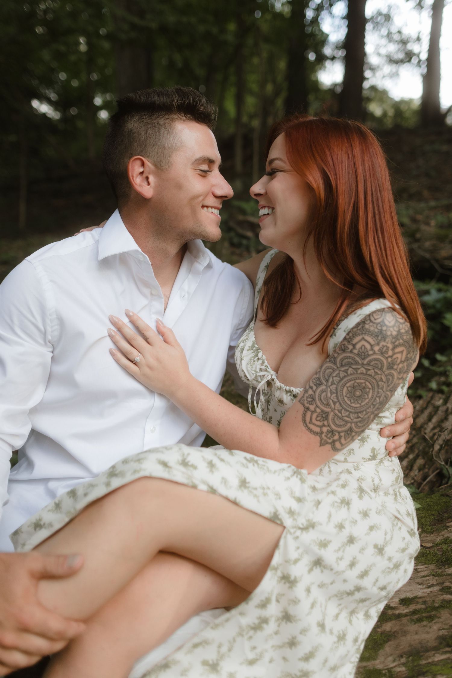 A couple sharing an intimate moment while sitting outdoors among trees.