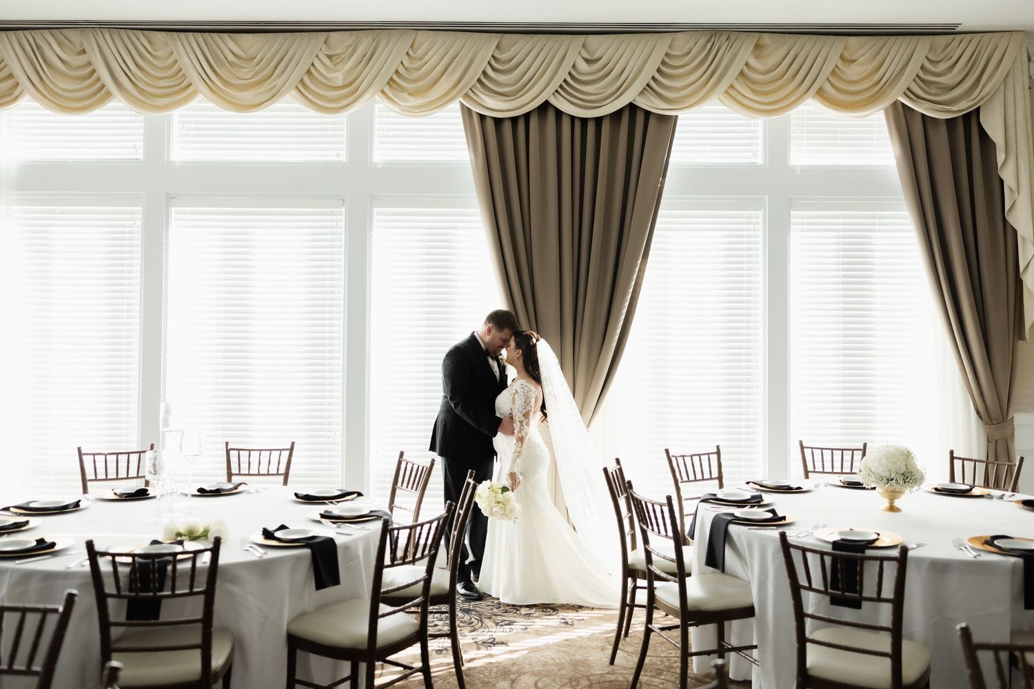 Elegant banquet hall with white tablecloths, dark chairs, and window drapes ready for formal dining service.