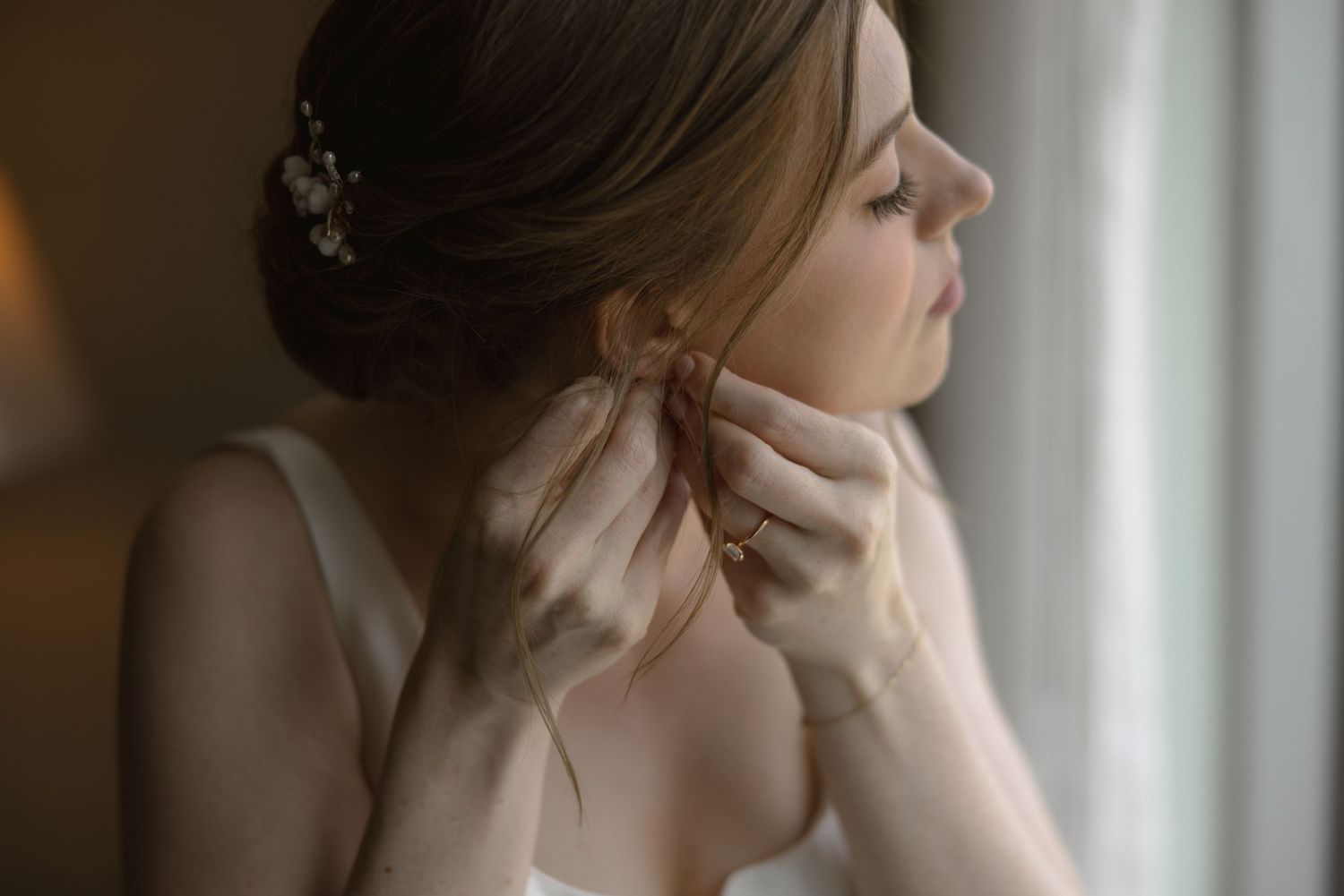 Elegant bridal preparation moment by window with soft natural lighting.