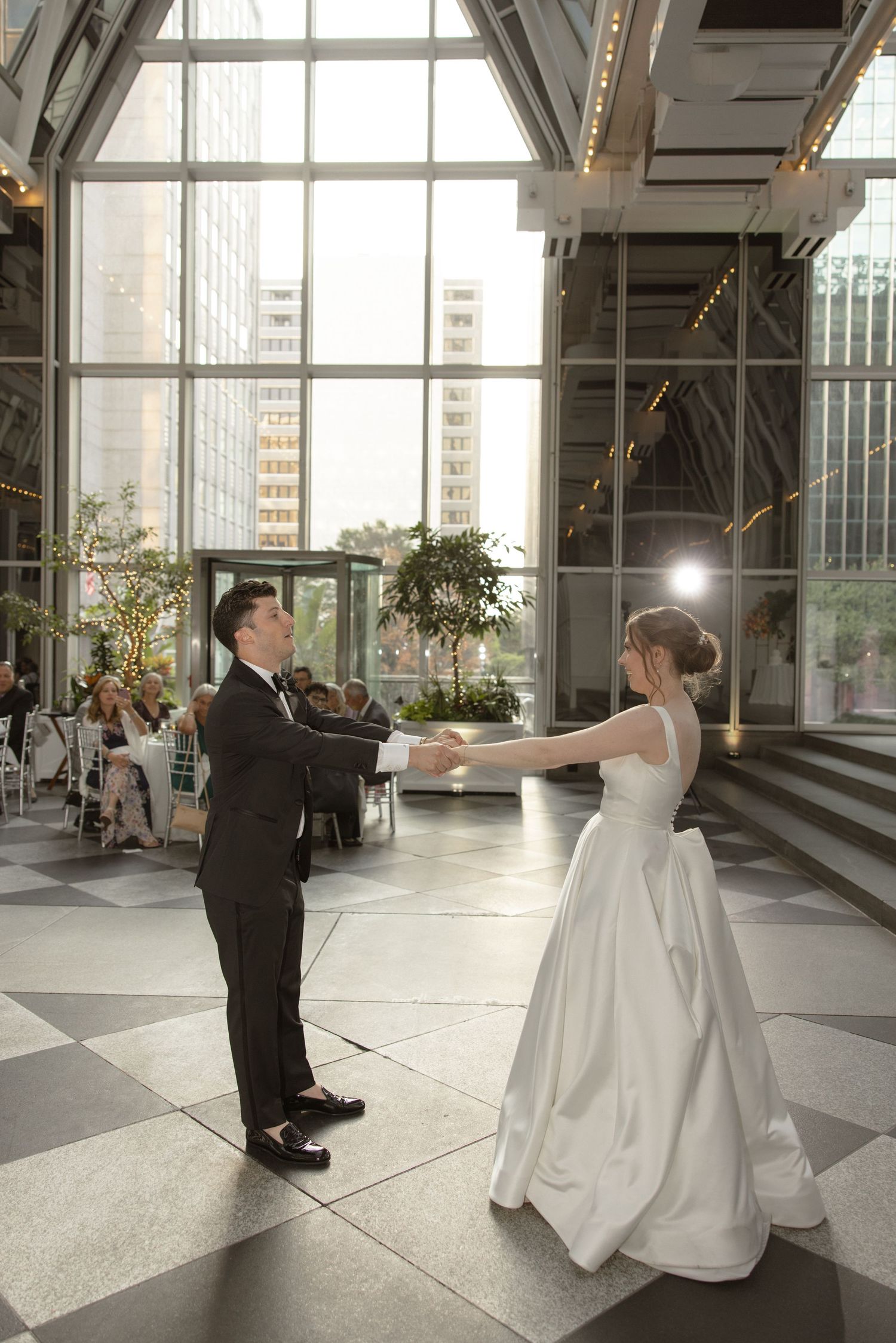 Couple sharing first dance in elegant venue with large windows and modern architecture.