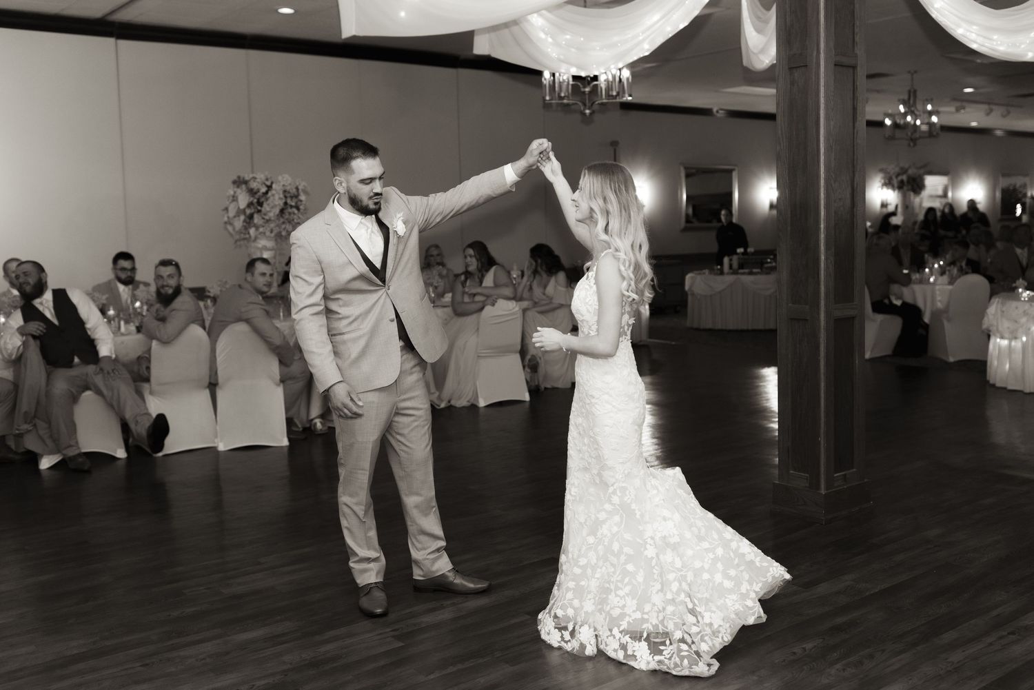 A couple shares their first dance in a spacious reception hall with elegant decor and ambient lighting.