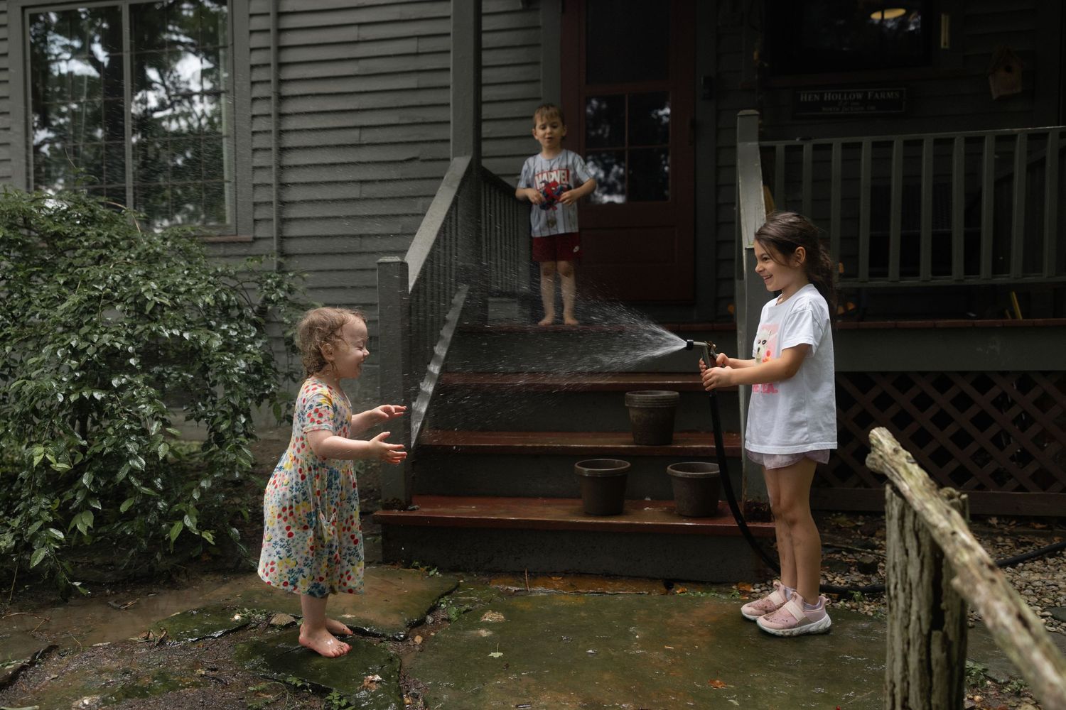 Child wearing a white t-shirt plays with soap bubbles on a porch during summertime.