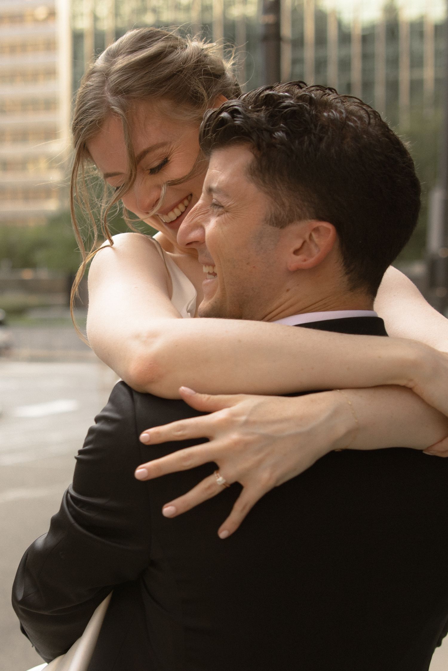 A joyful embrace outdoors against an urban backdrop with warm lighting and tender emotion.