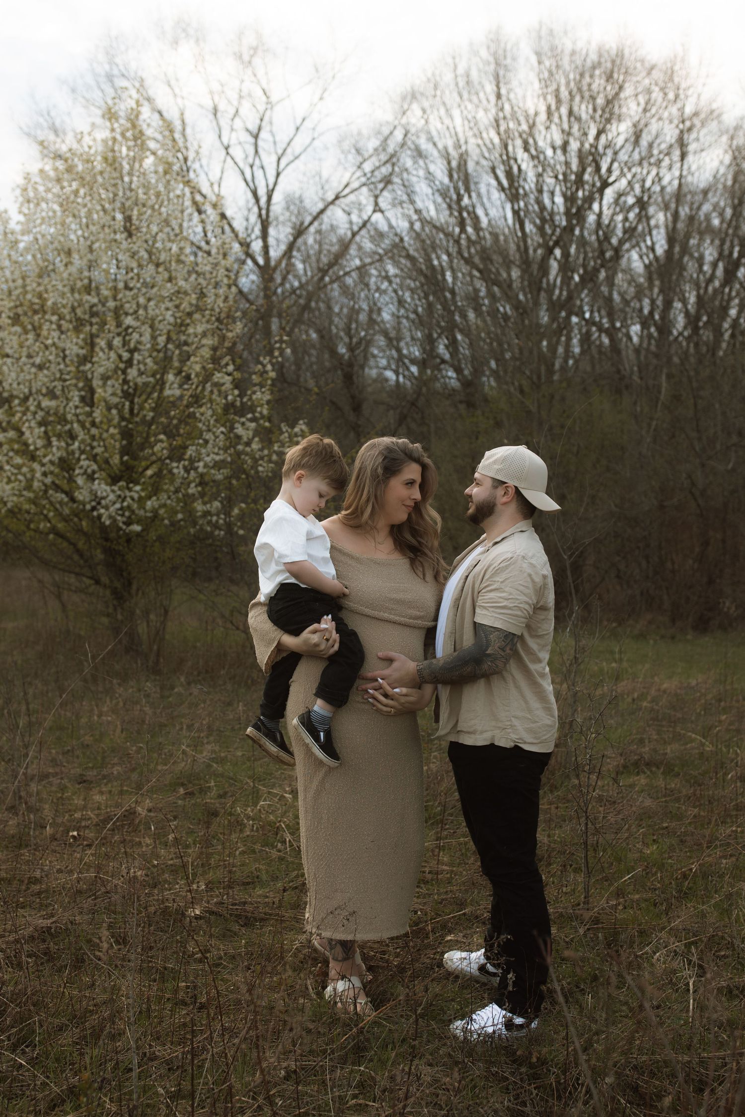 Family portrait in natural setting with blooming trees and neutral colored clothing.