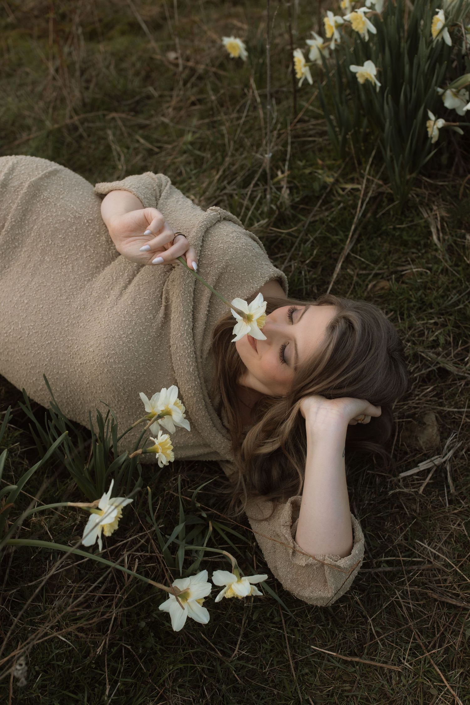 A relaxed maternity portrait among blooming daffodils in a garden setting.