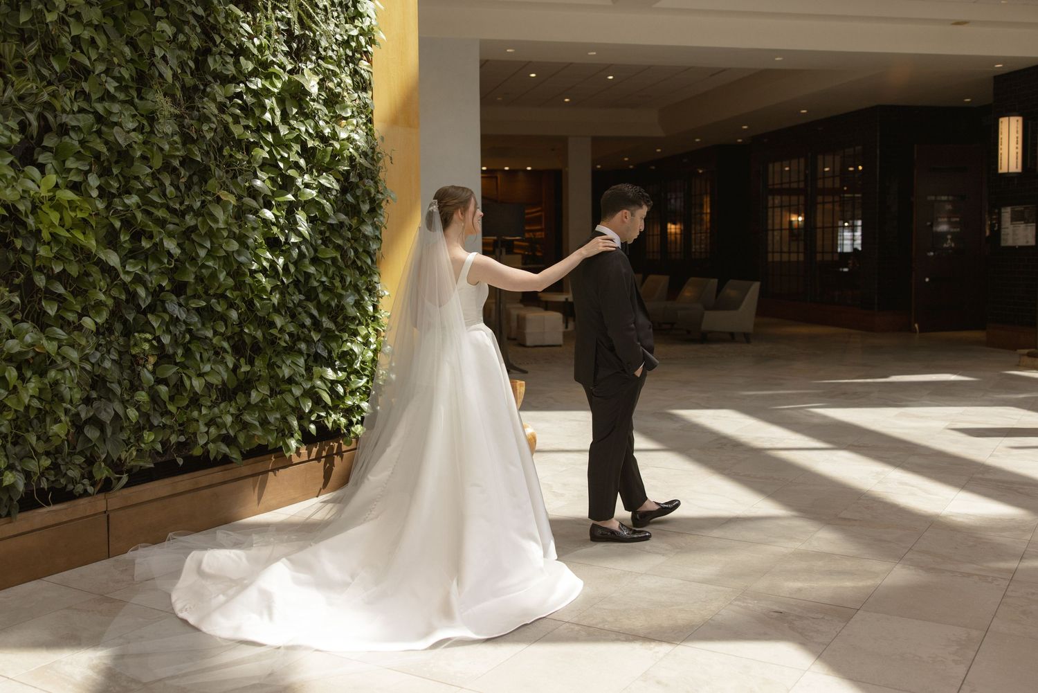 Bride and groom share a first look moment in a sunny hallway with living plant wall.