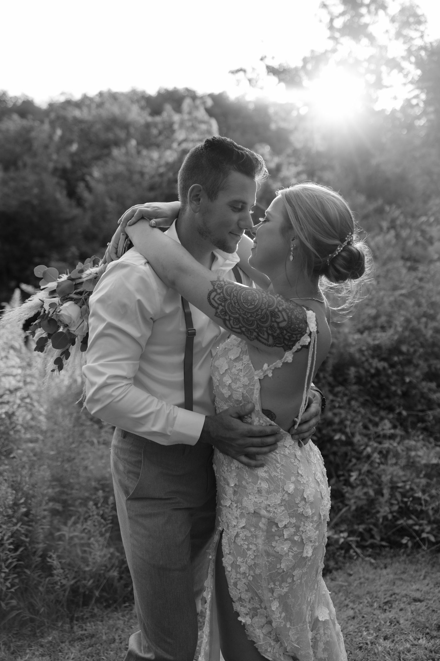 A couple shares an intimate dance pose in nature during sunset with the sun creating a beautiful backlit glow through the trees.
