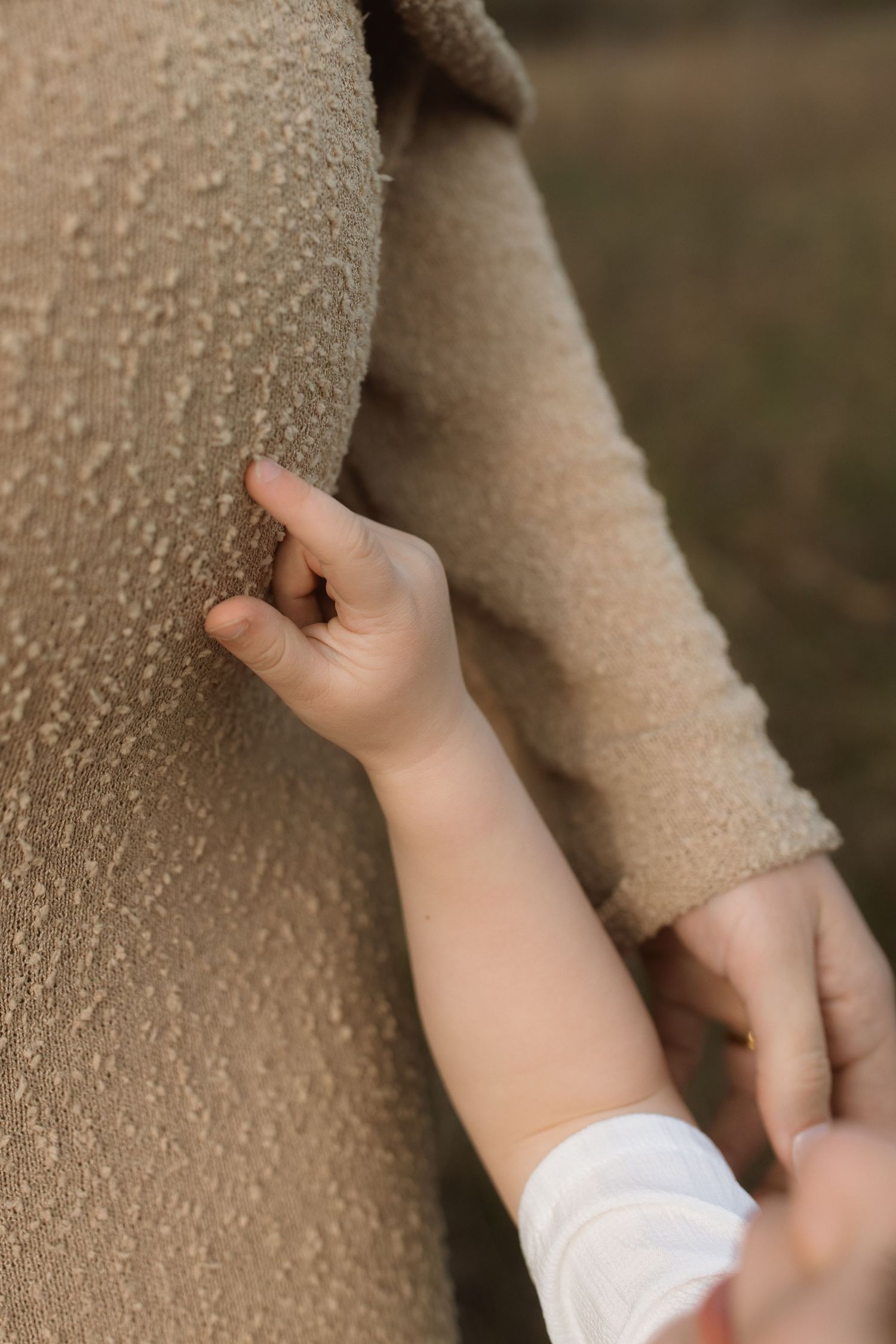 Close-up of small child's hand touching textured beige fabric.