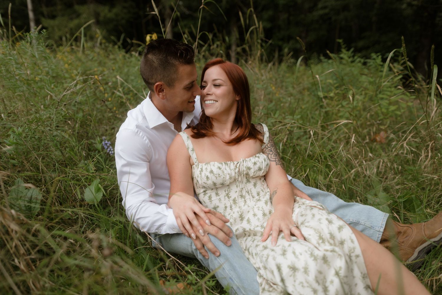 A couple sits intimately together on a blanket in a grassy outdoor setting during a summer afternoon.