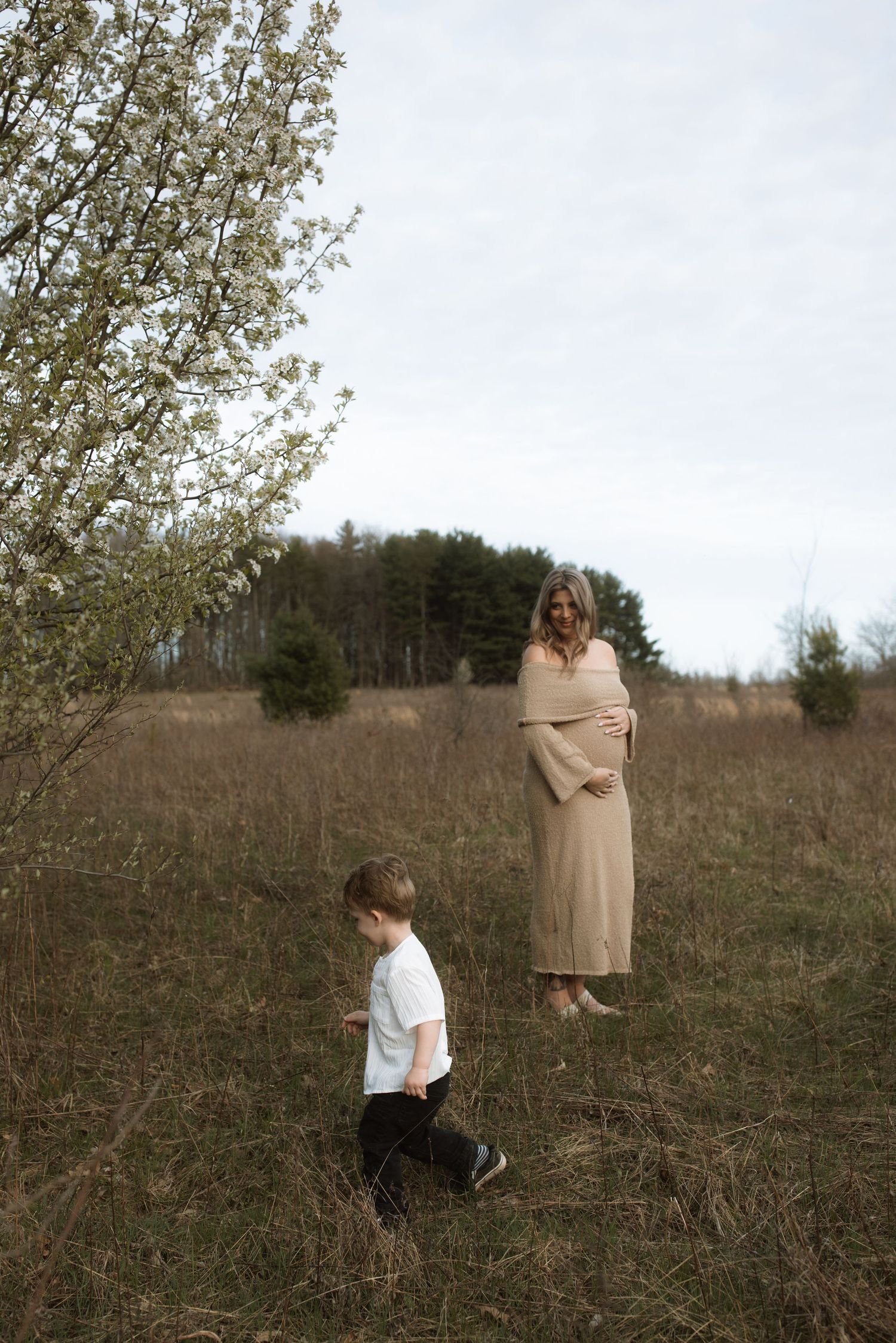 A rustic outdoor maternity photo session in a field with flowering trees.