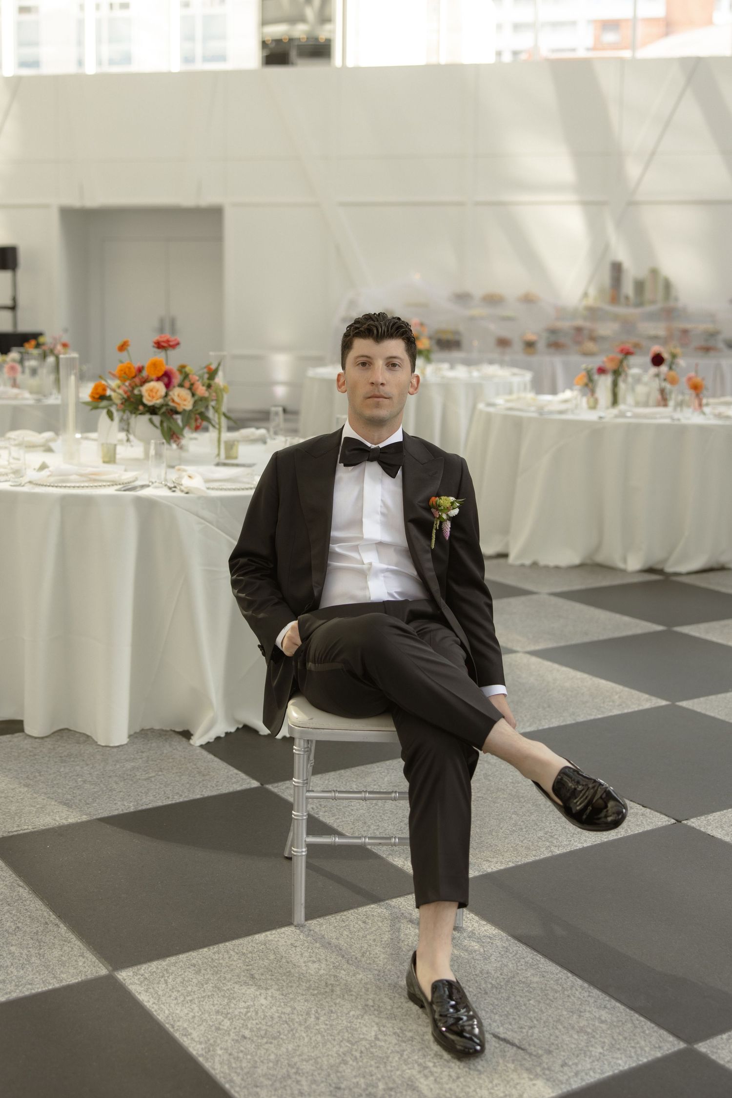 Wedding attire featuring a dark tuxedo with loafers in a modern reception space.