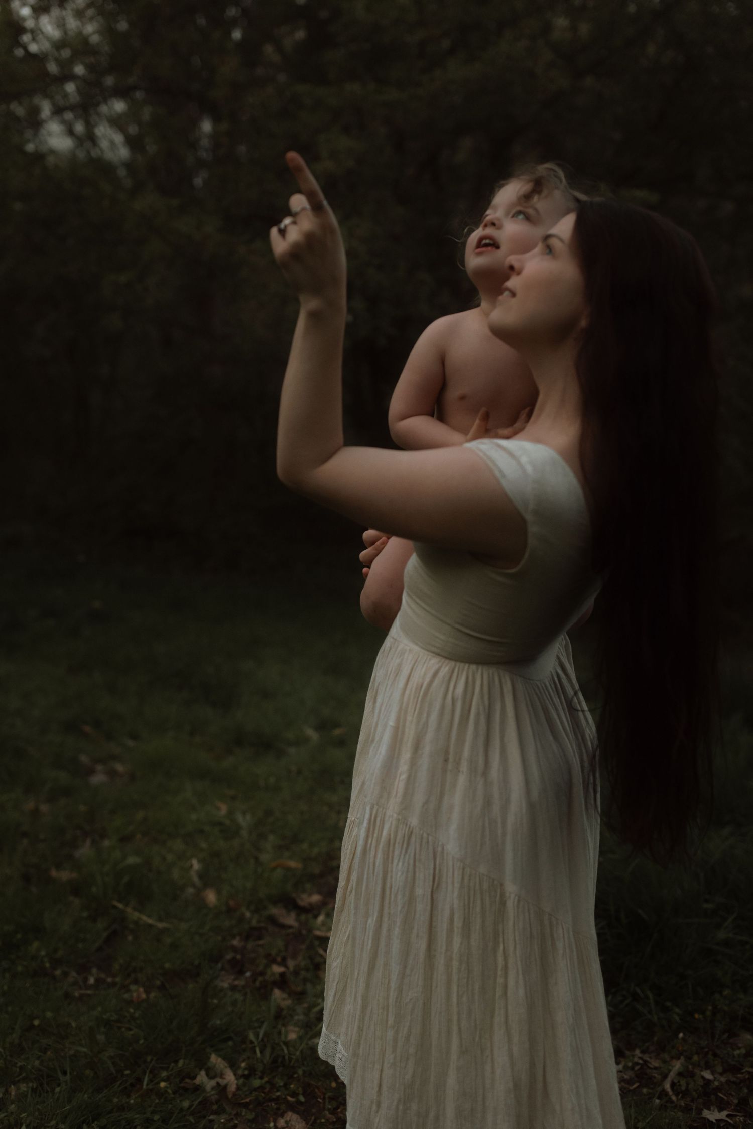 A figure in white reaches skyward in a moody forest setting at dusk.