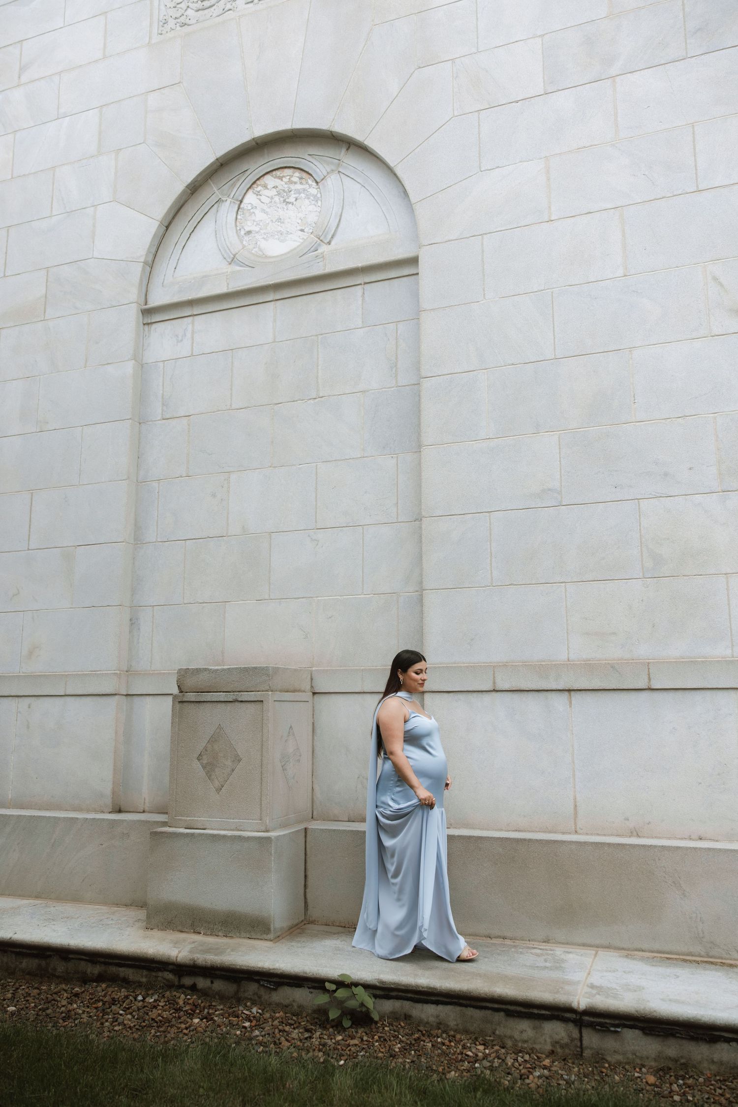 Figure in flowing blue dress against textured stone wall architecture.