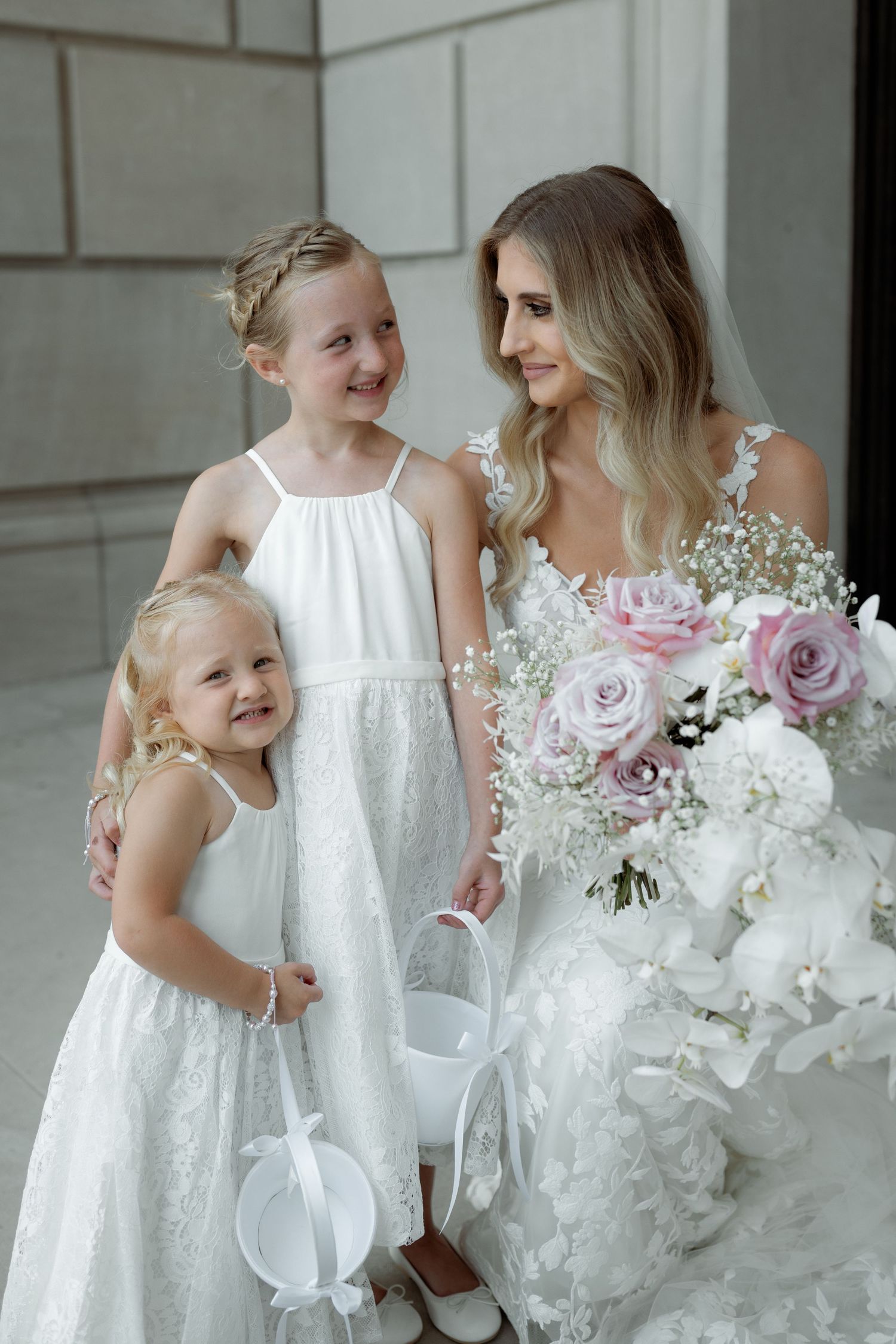 A wedding party with flower girls in white dresses poses with beautiful pink and white floral bouquets.