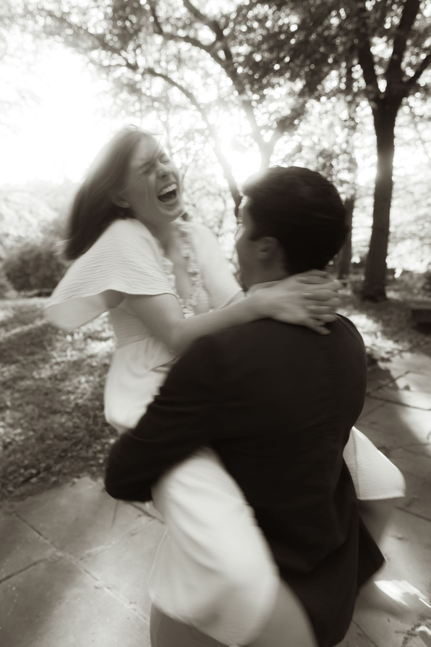 A joyful couple spins and embraces in a romantic black and white outdoor photo captured in soft focus.