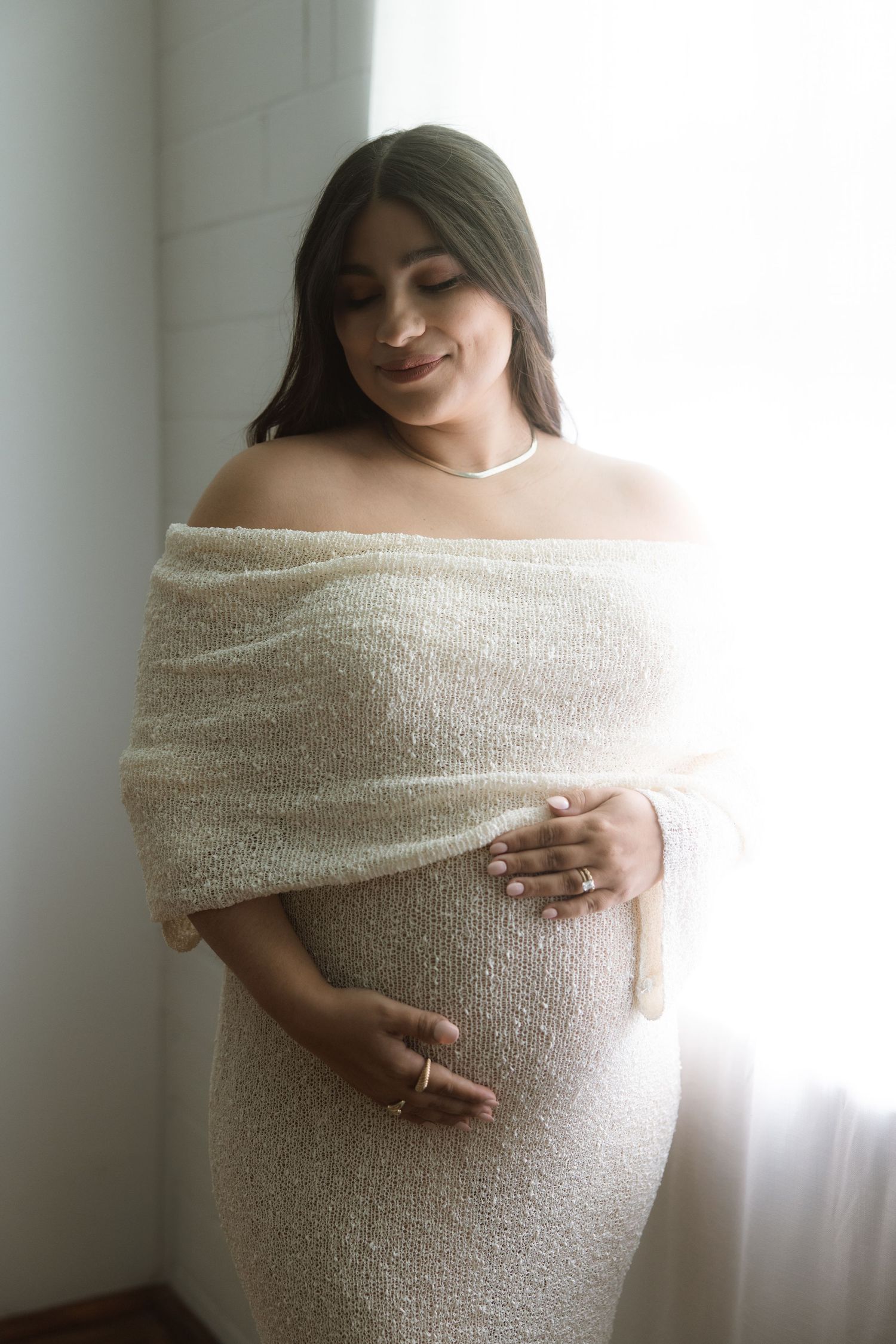 Maternity photoshoot featuring a light wrapped fabric and soft window lighting.