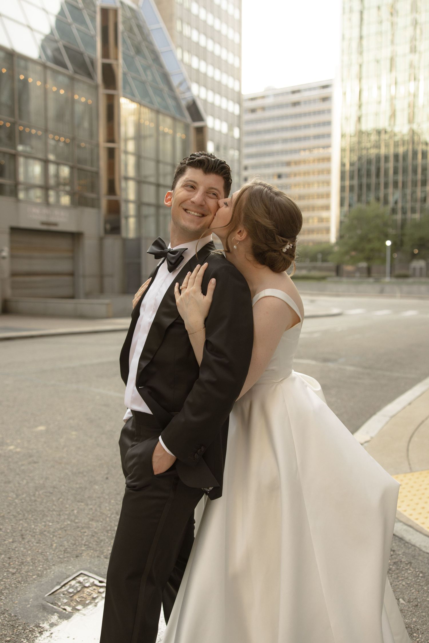 A candid wedding moment between a couple in formal attire on a city street.