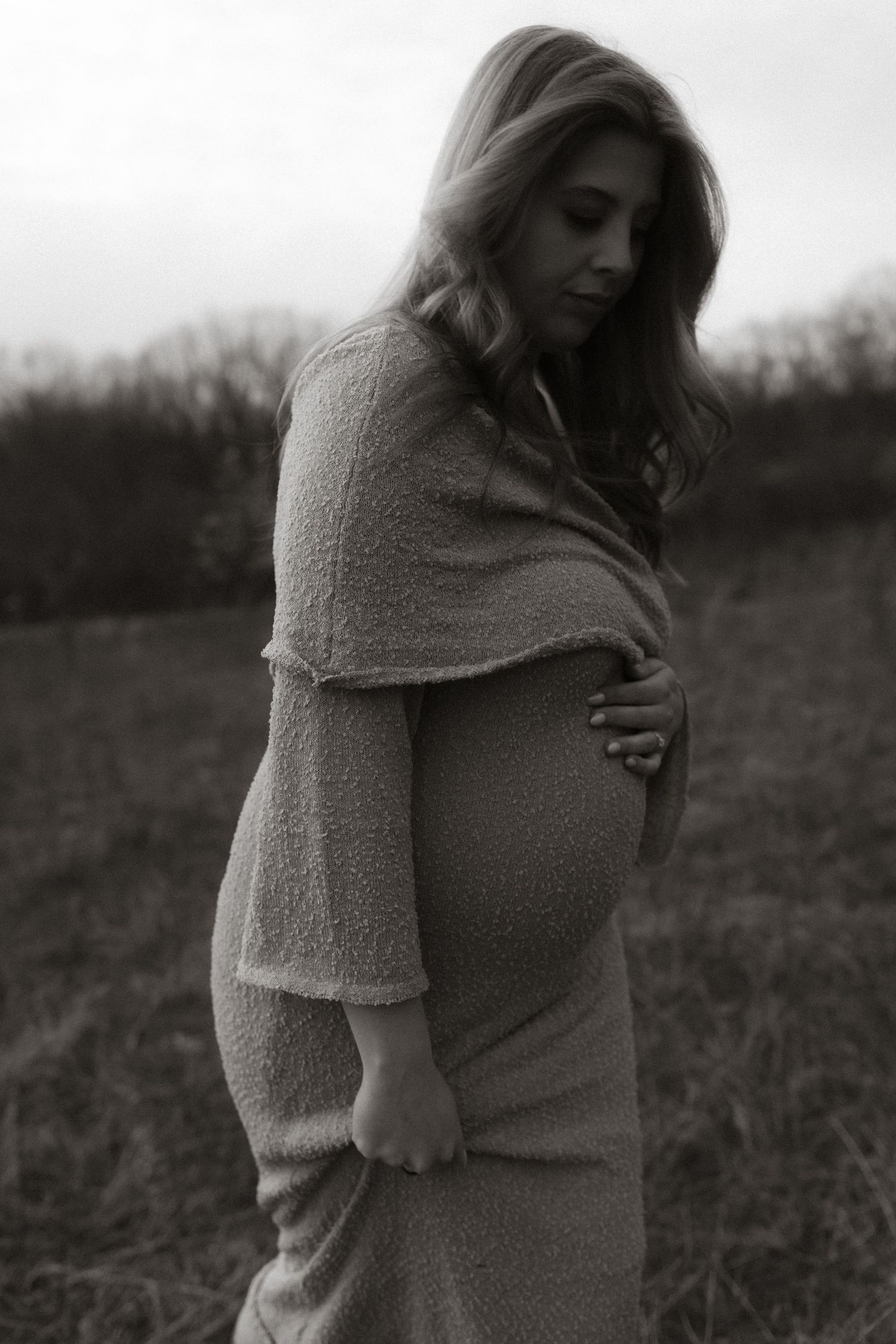 Black and white maternity portrait in a field wearing a soft knit dress.