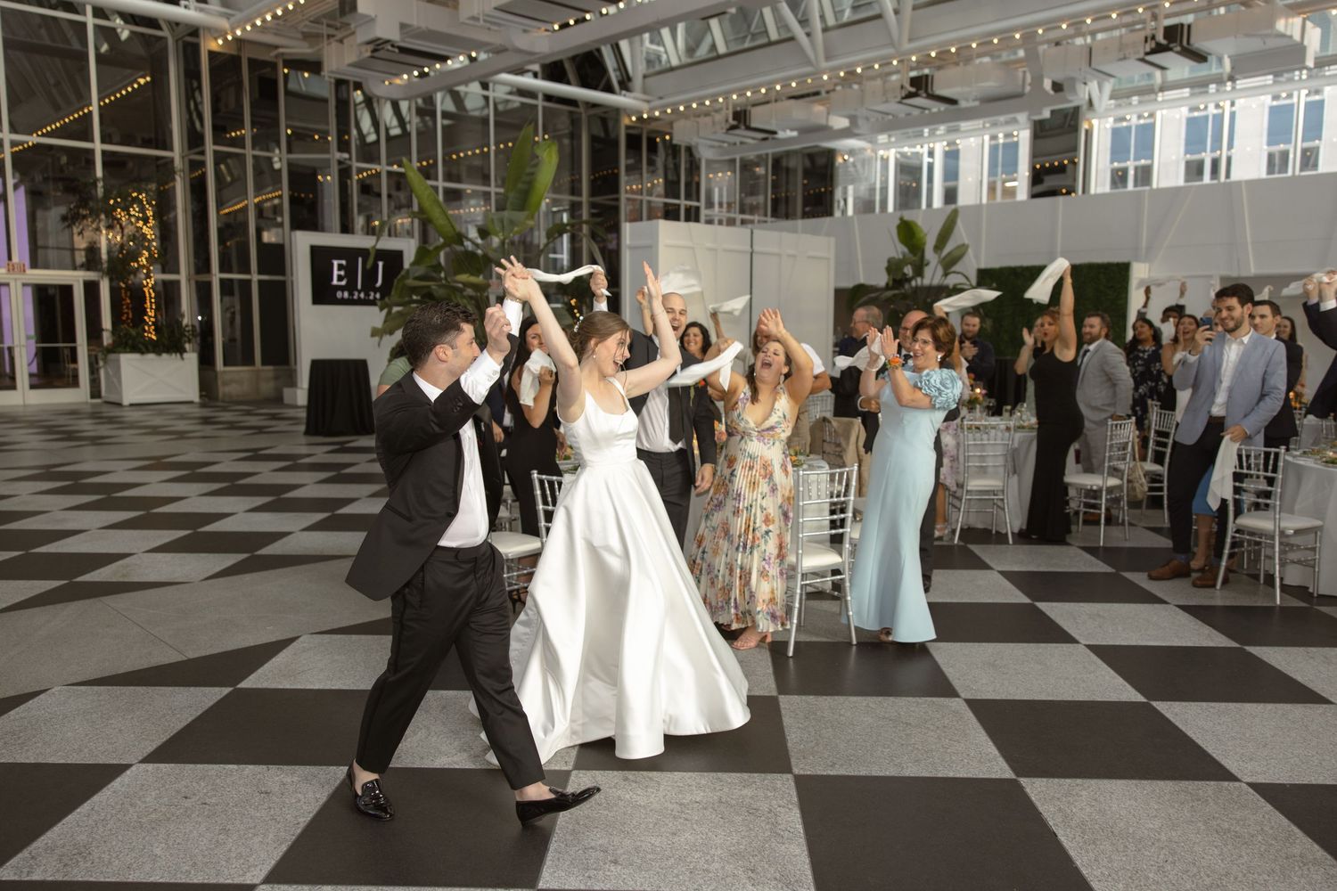 Wedding couple dancing with guests on checkered floor at modern venue reception celebration.