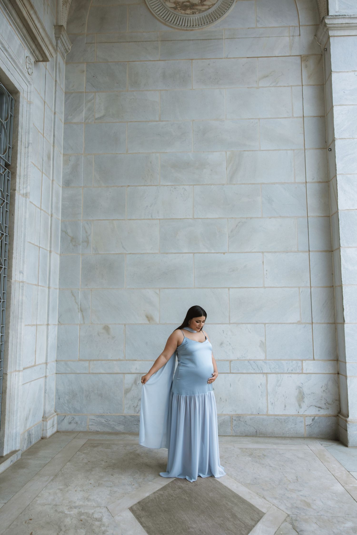 A person wearing a light blue dress twirls and dances in an elegant marble-columned space.