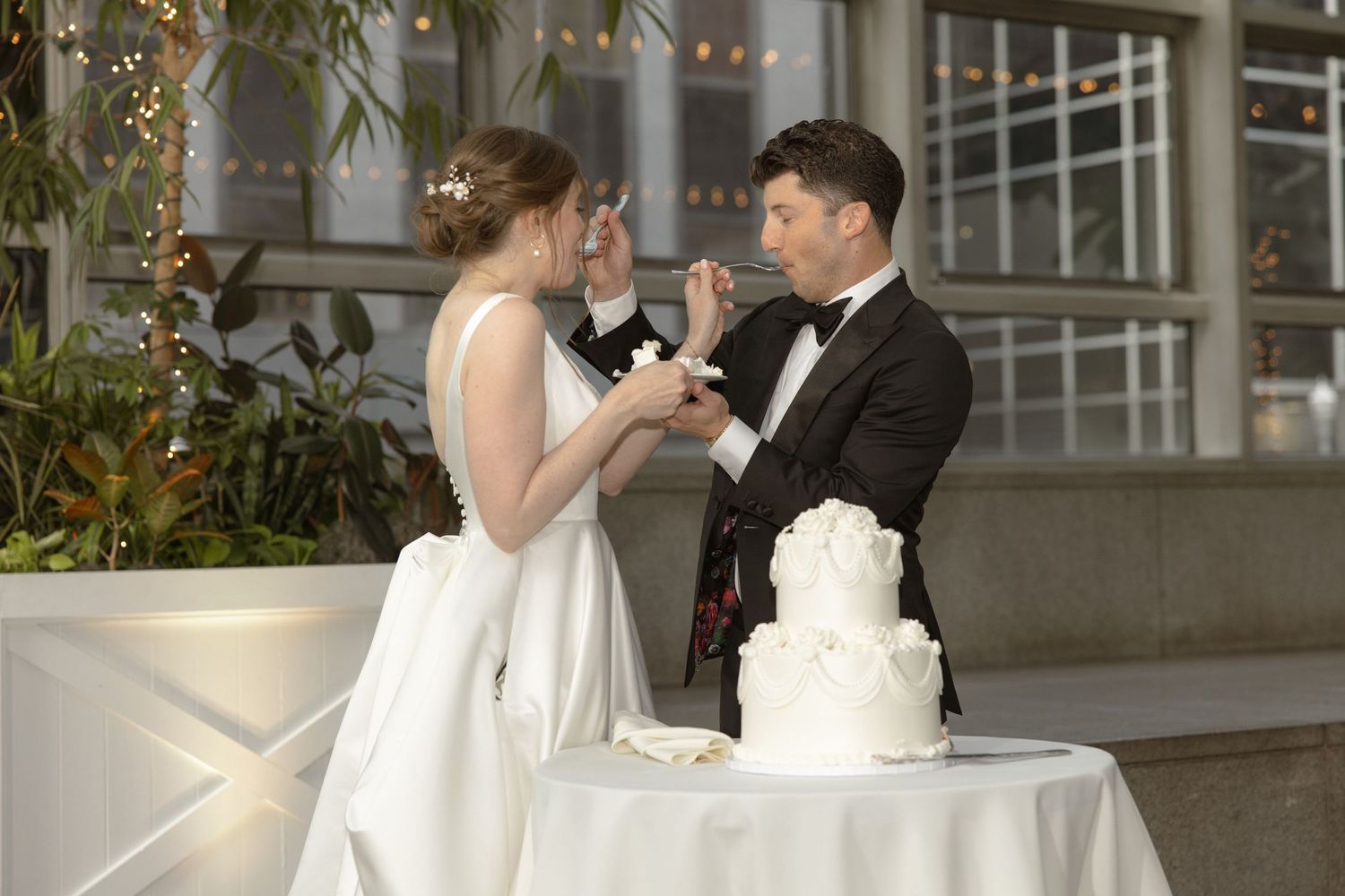 Newlyweds sharing cake and smiling at modern wedding reception venue.