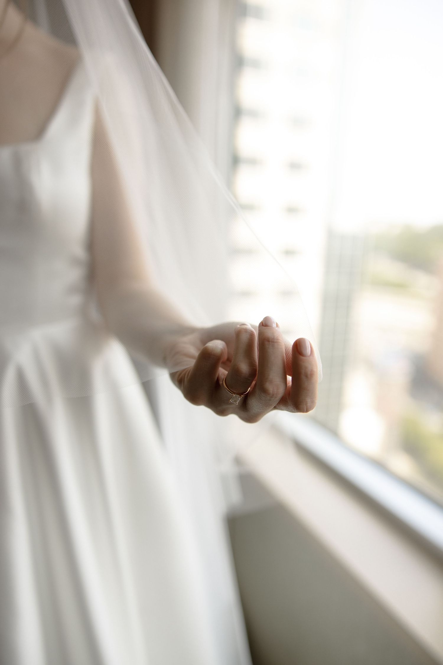Close-up view of hands wearing delicate wedding jewelry near a bright window.