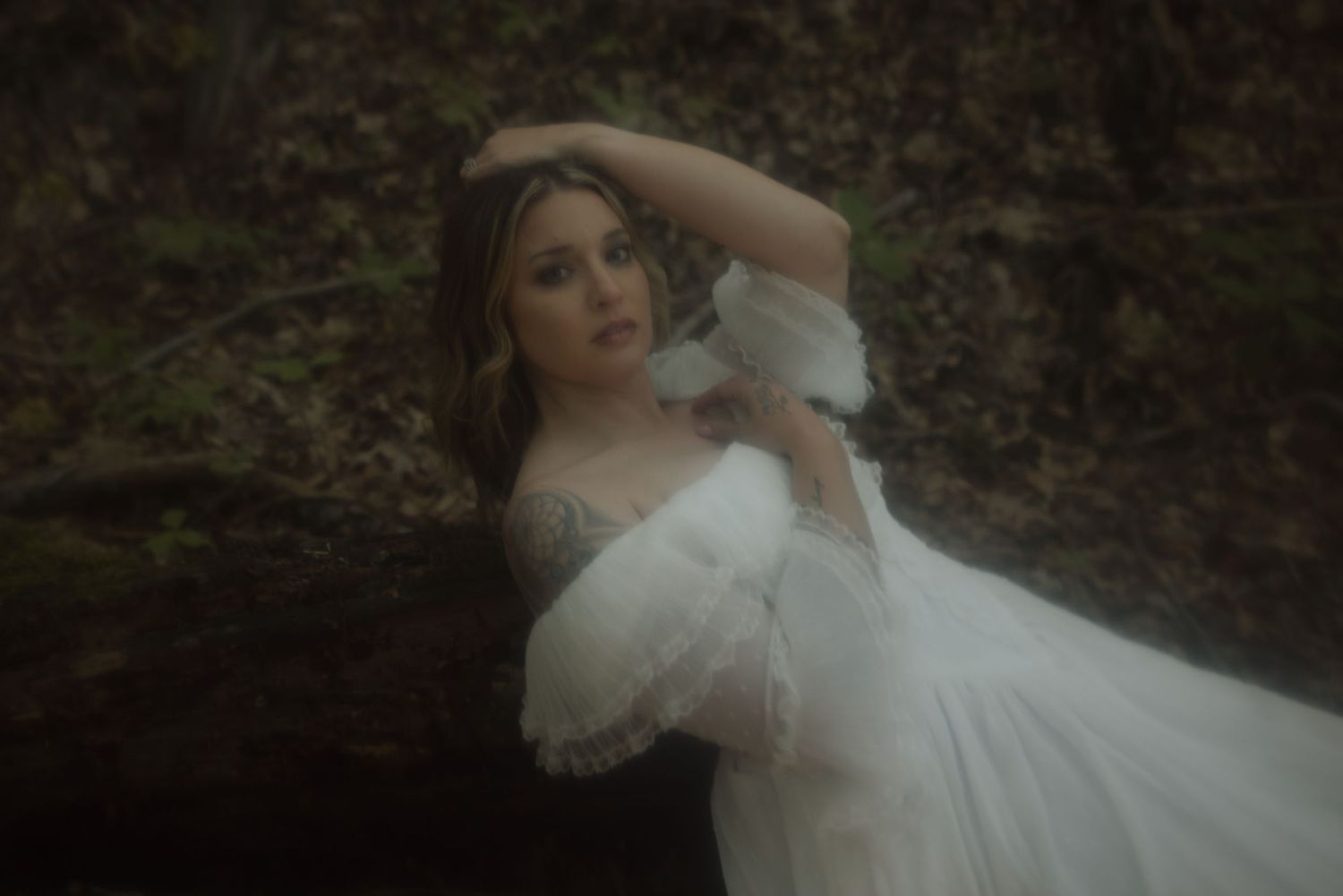 Dreamy portrait of a person in a flowing white dress posing elegantly in a misty forest setting.