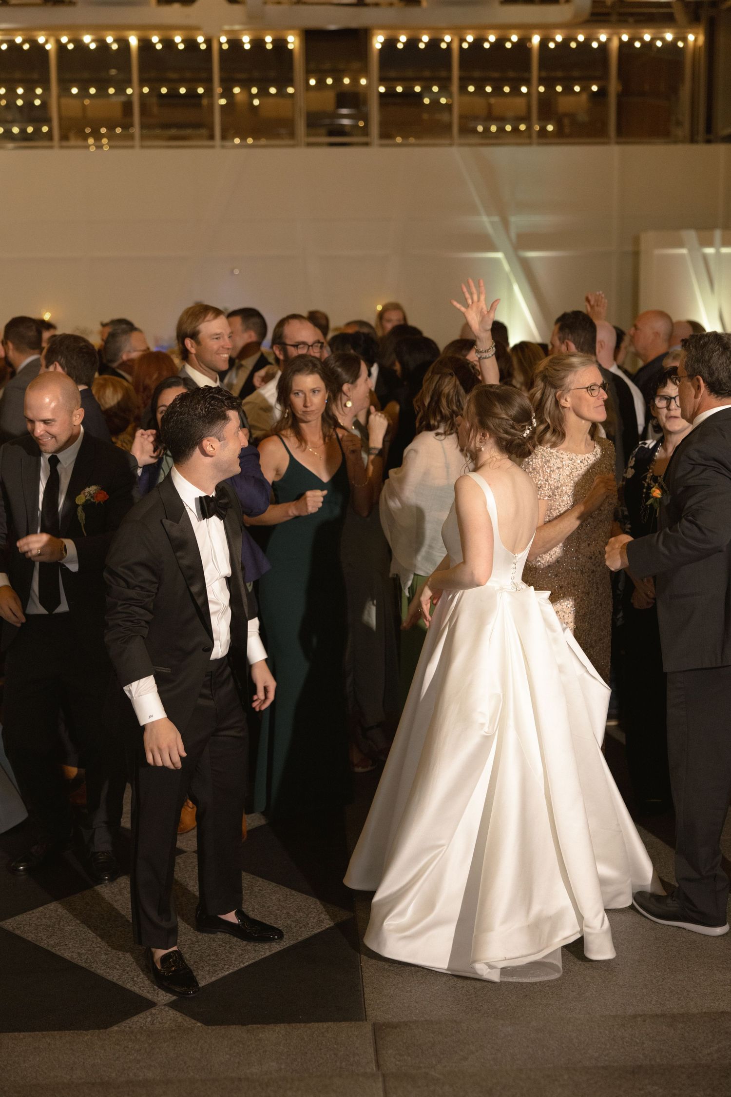 Wedding reception dance party with guests in formal attire under string lights.
