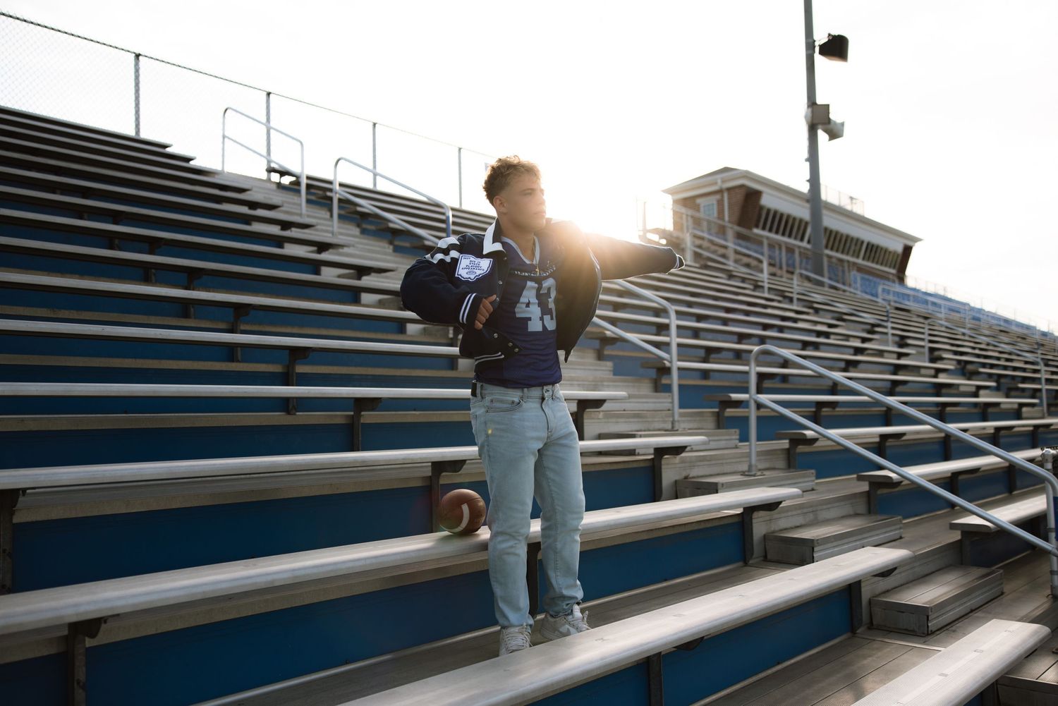 Student standing alone in empty stadium bleachers during sunset with backpack and light flare behind.
