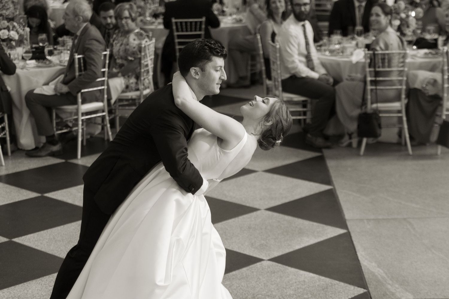 Black and white photo of couple performing dramatic dip during wedding dance on checkered floor.