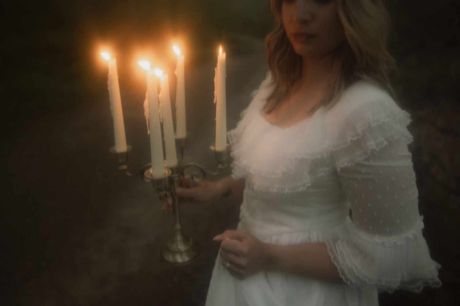 A person in a flowy white dress holds lit candles in a darkened setting, creating a romantic ambiance.
