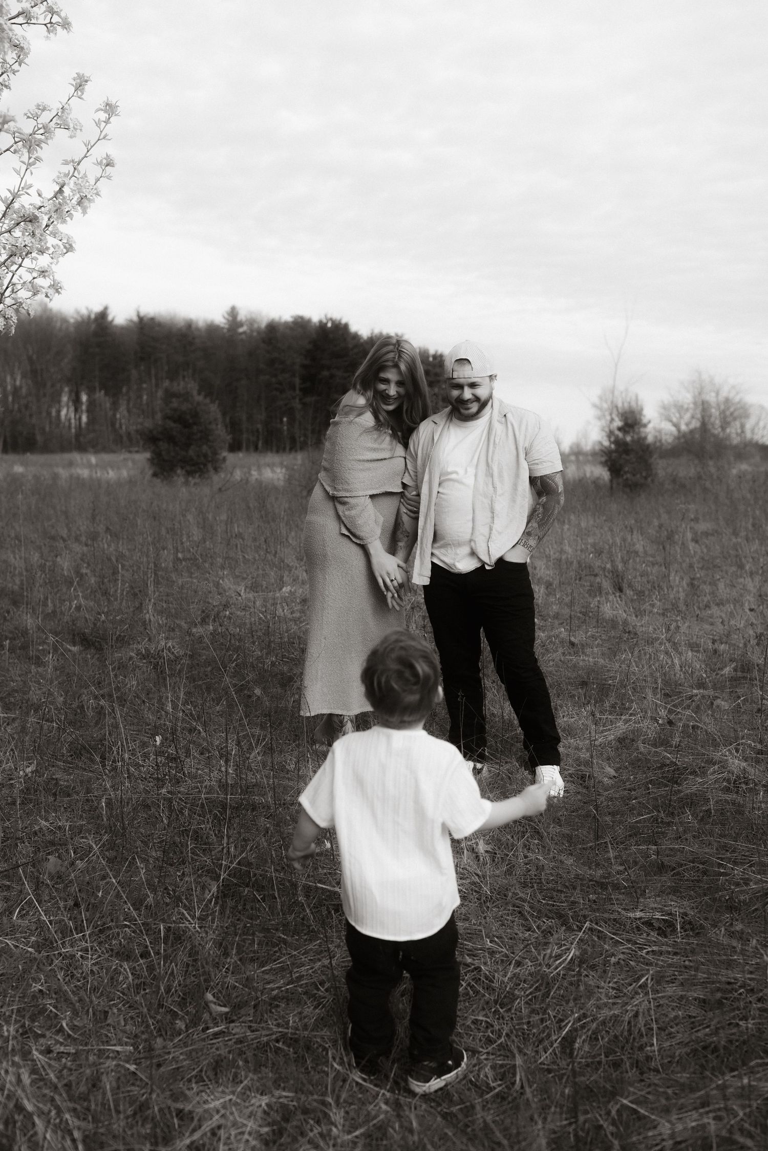 A black and white family portrait in an open field with blooming trees.