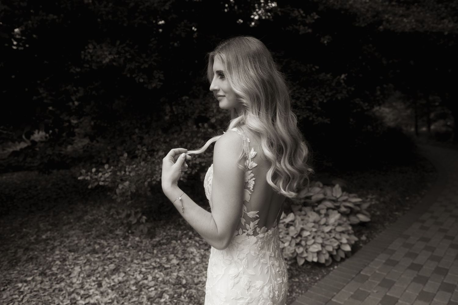 Black and white portrait of bride in lace gown with long flowing hair in outdoor garden setting.
