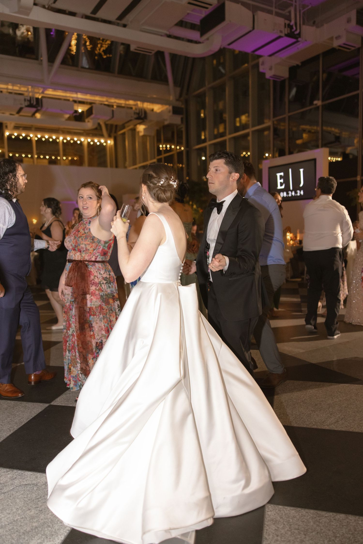 A wedding reception scene with guests dancing under string lights in an industrial-style venue.