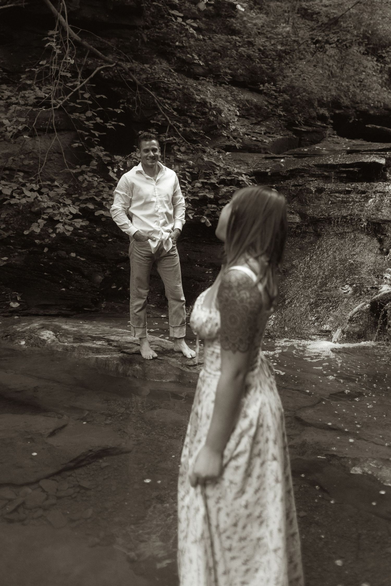 A black and white photo of a couple standing near rock formations in a natural setting.