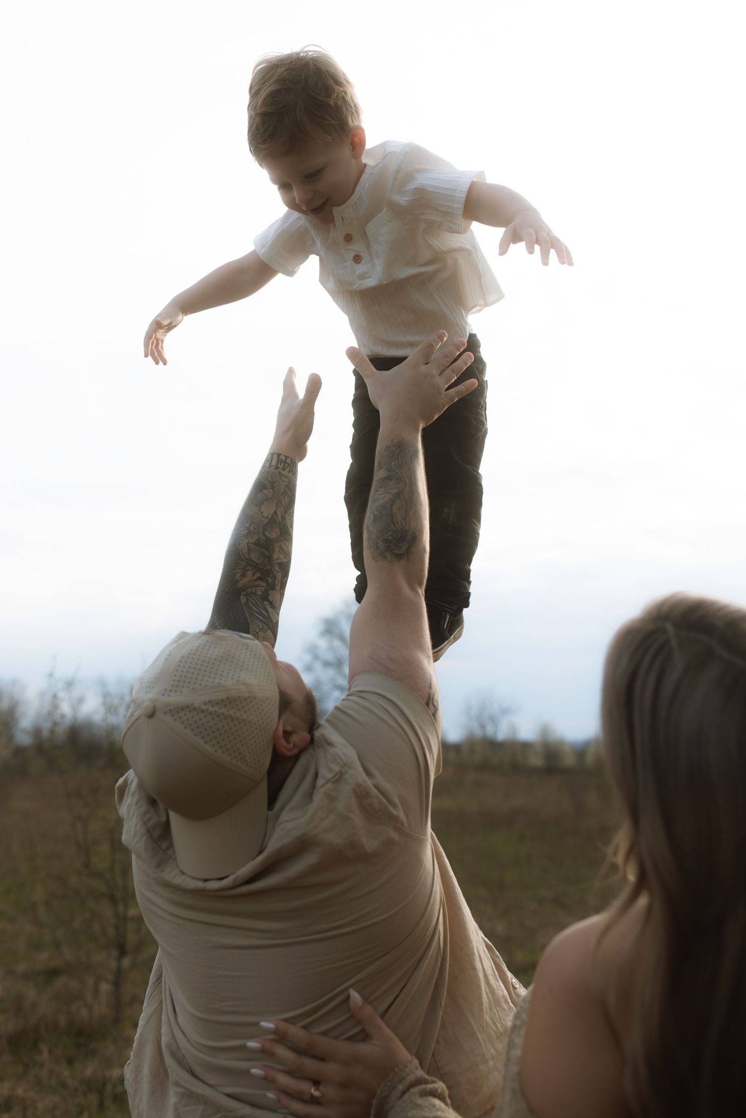 Playful moment of lifting child high in the air against bright sky backdrop.