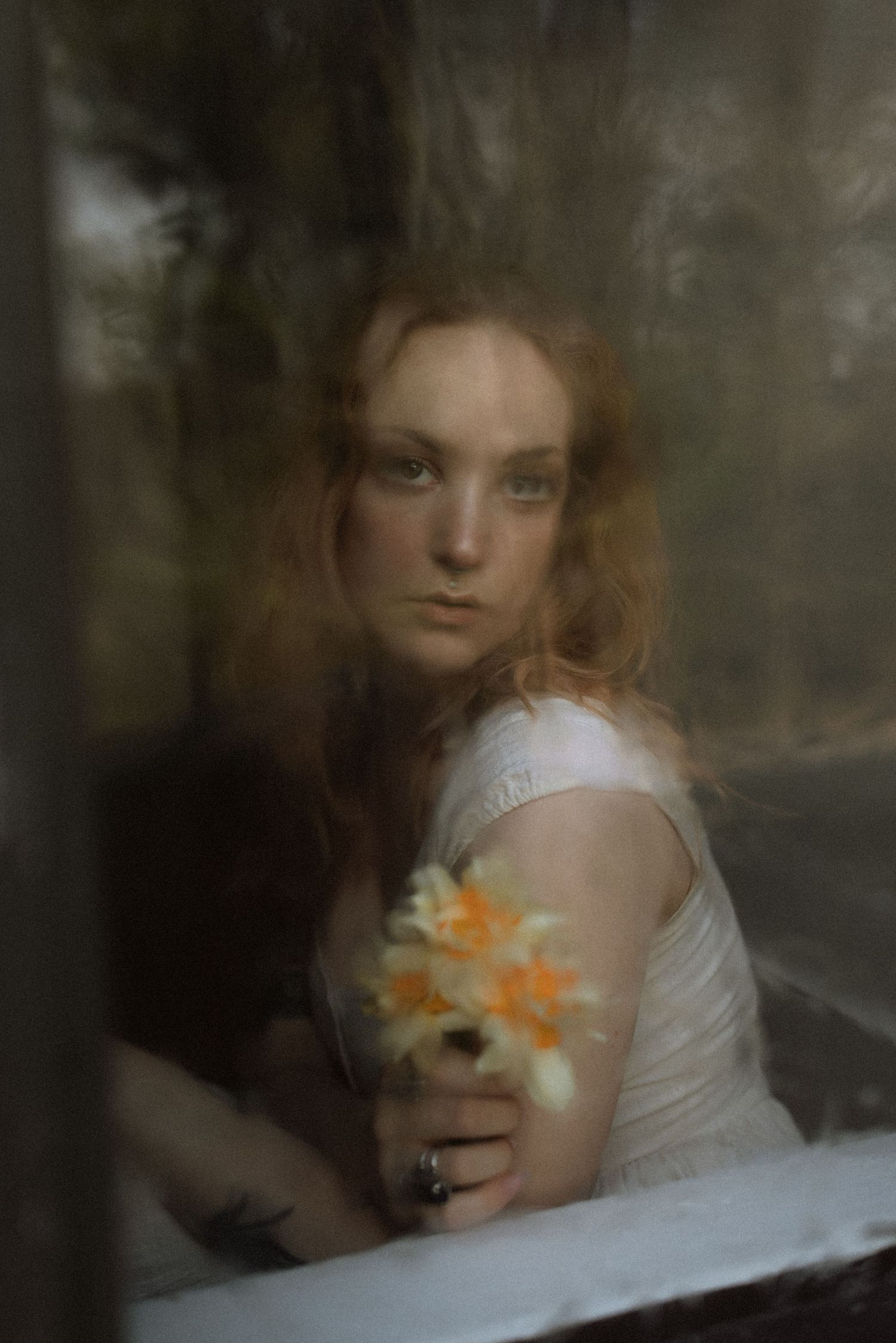 Dreamy artistic portrait through window with white dress and yellow daffodils creating ethereal romantic atmosphere.