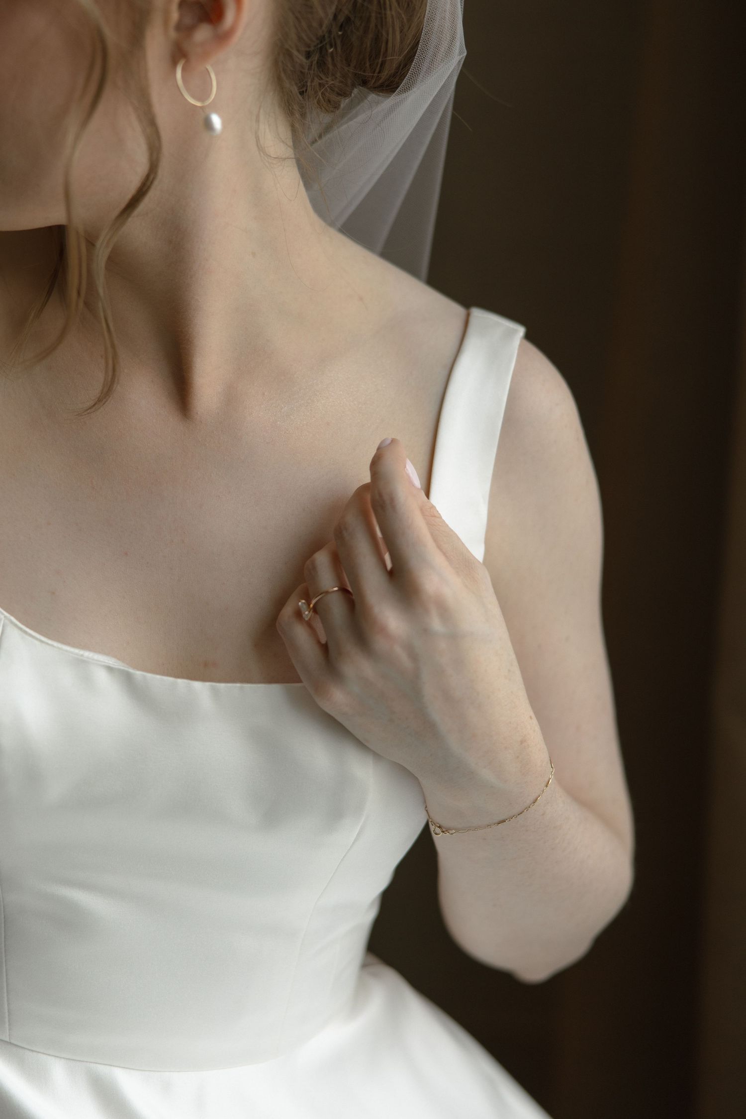 Detail shot of wedding dress strap and jewelry against soft lighting.
