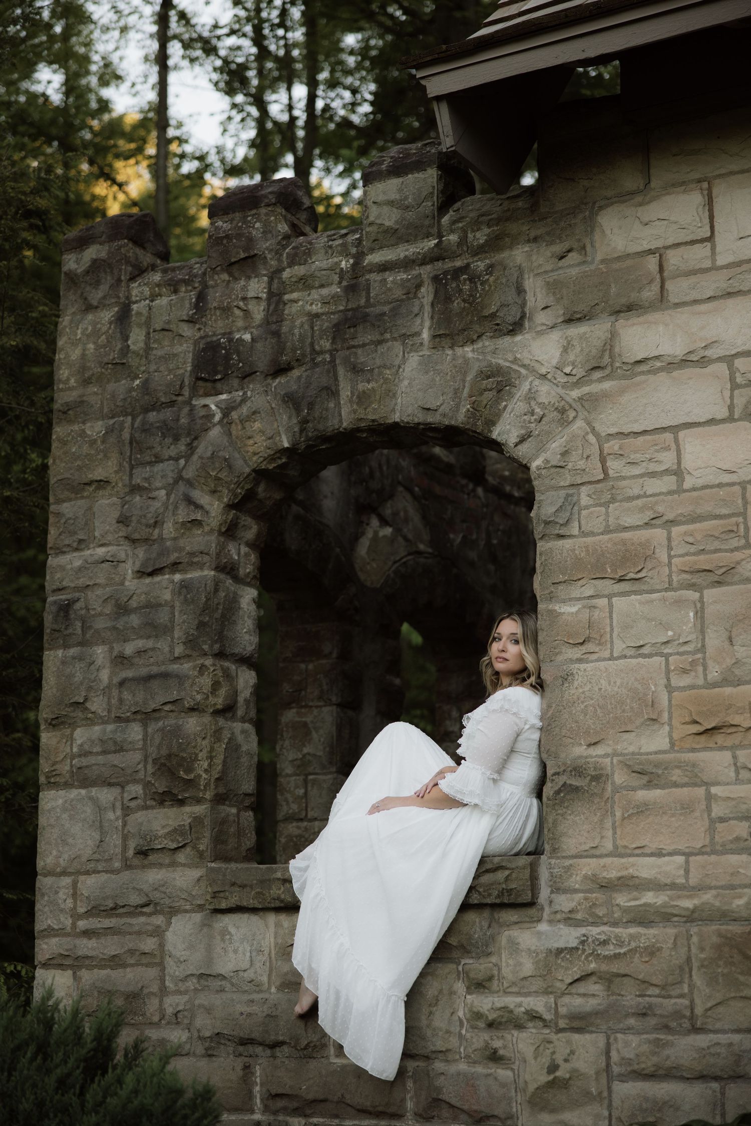 A white lace dress cascades elegantly as someone sits in a stone archway at dusk.