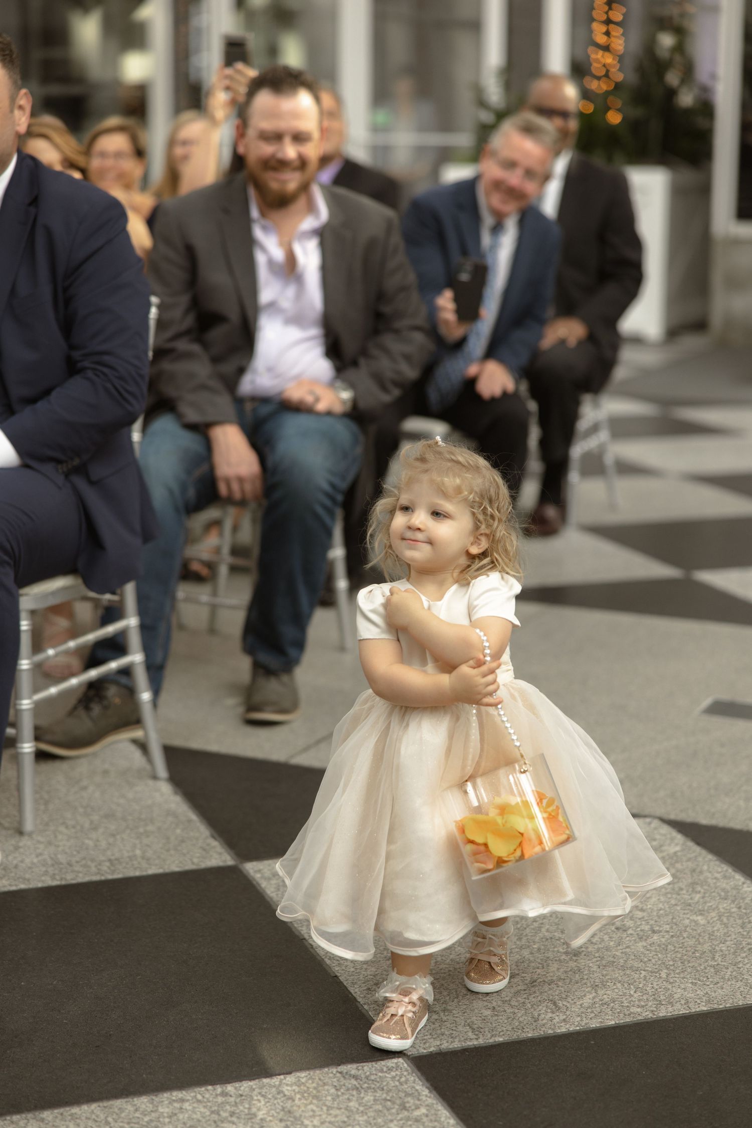 Flower girl in tulle dress carrying basket during wedding ceremony.
