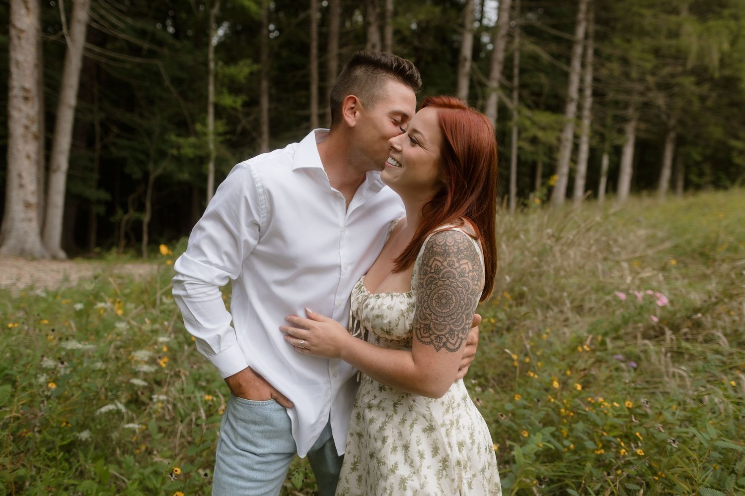 A couple shares an intimate moment together in a forest setting wearing white attire during golden hour light.
