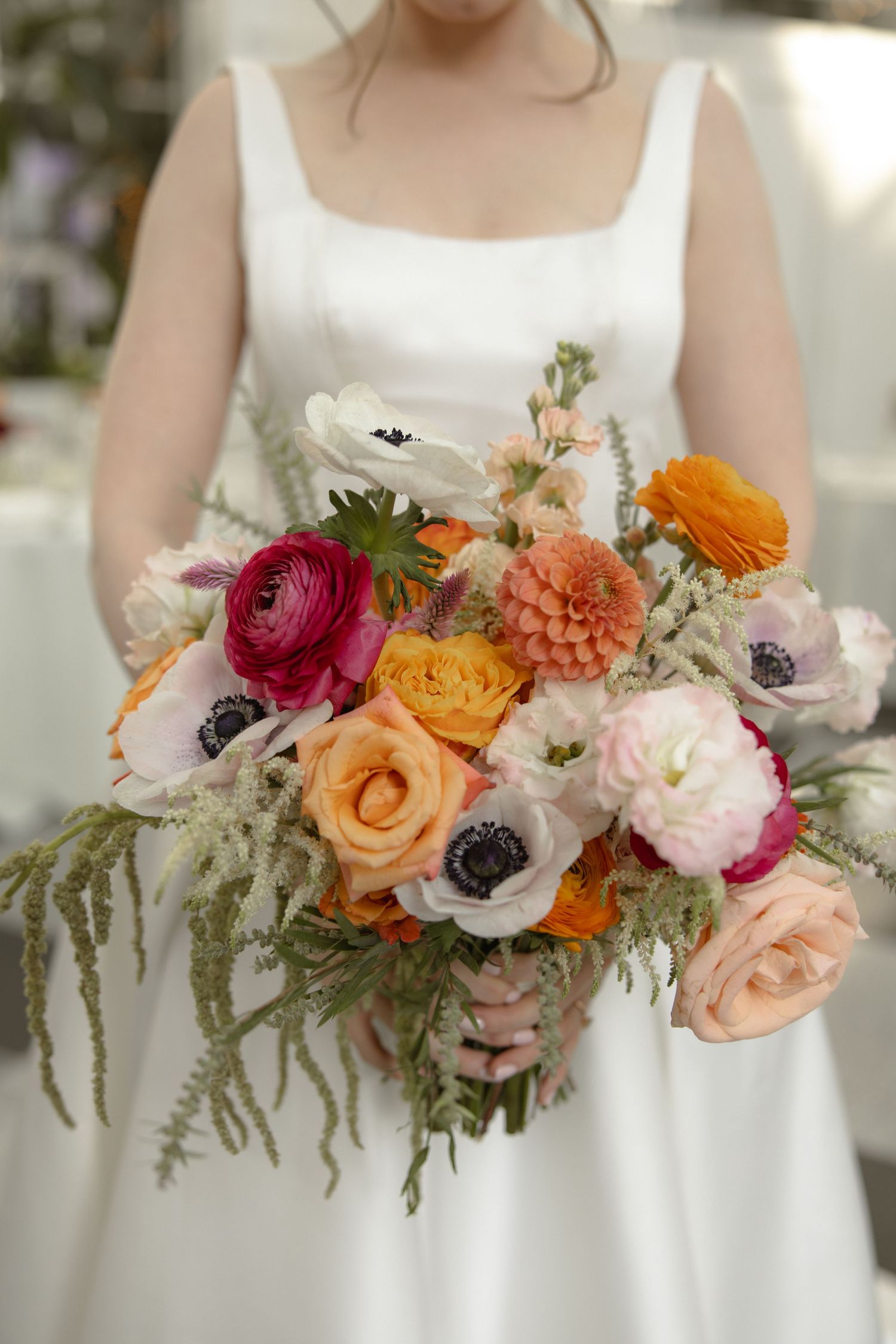 Colorful bridal bouquet with pink, orange, and white flowers against a white dress.